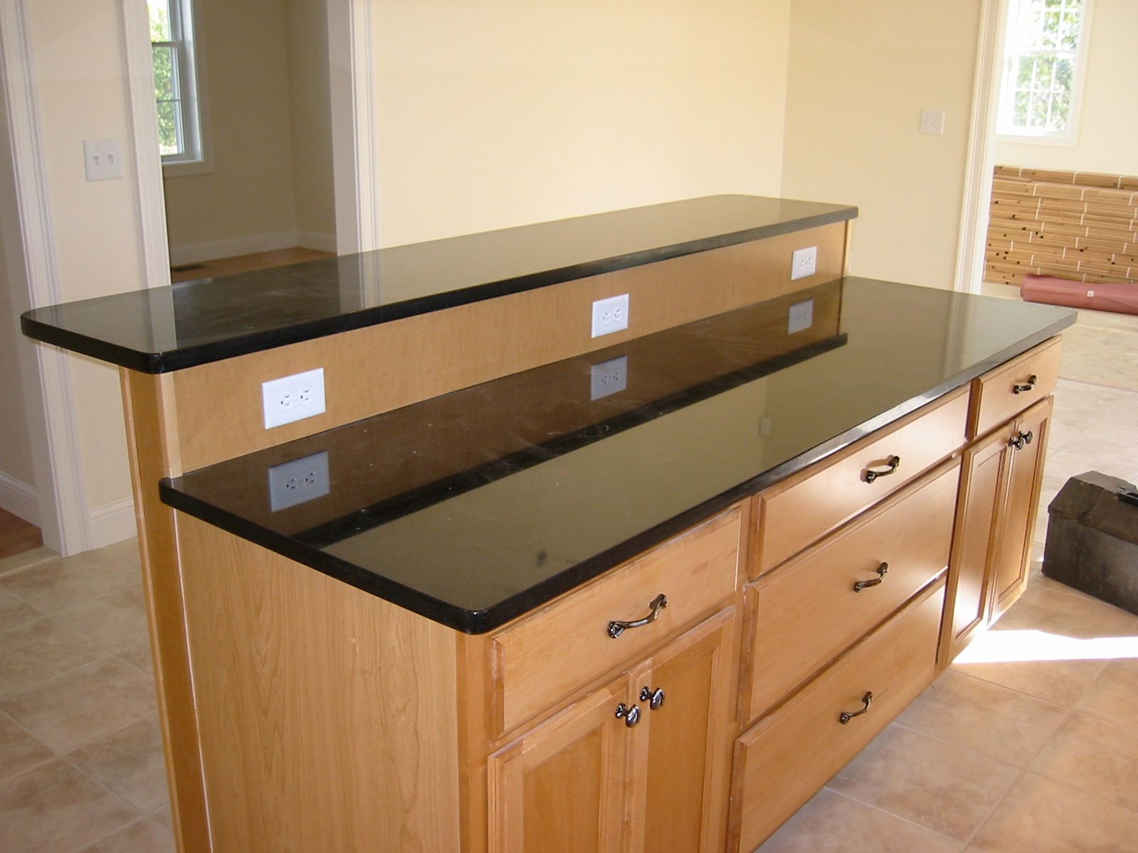 Kitchen island with black granite countertop, light wood cabinets, and built-in electrical outlets.