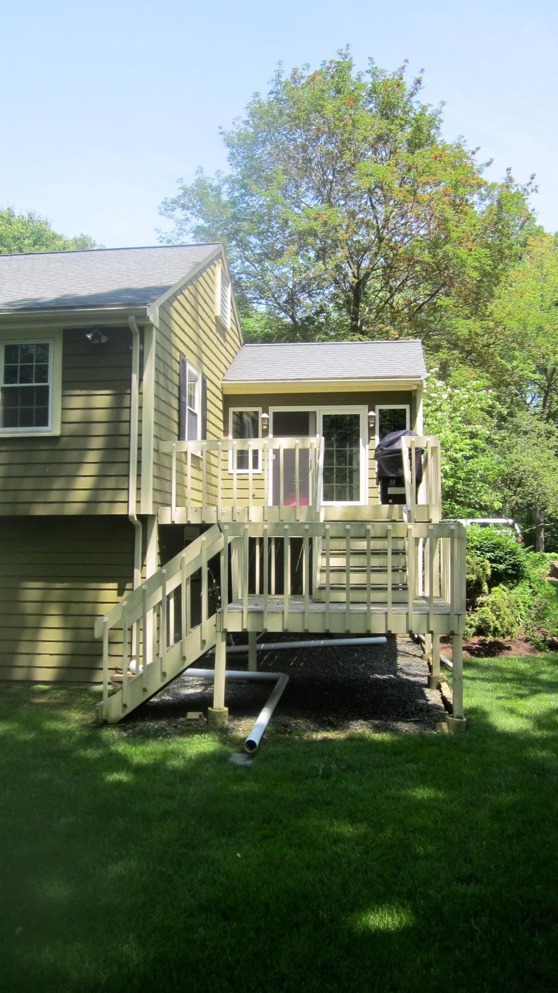 A green house with a wooden deck, stairs, and a screened-in porch, viewed from the yard.