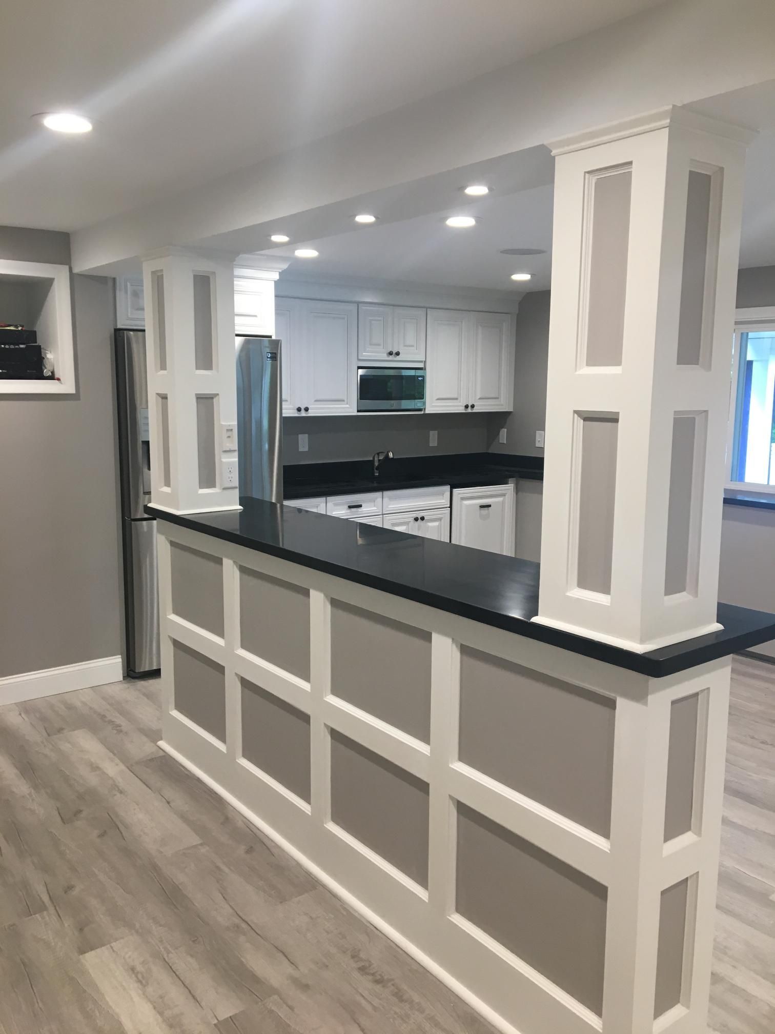 Kitchen with white cabinets, black countertop bar, gray and white paneled accents.