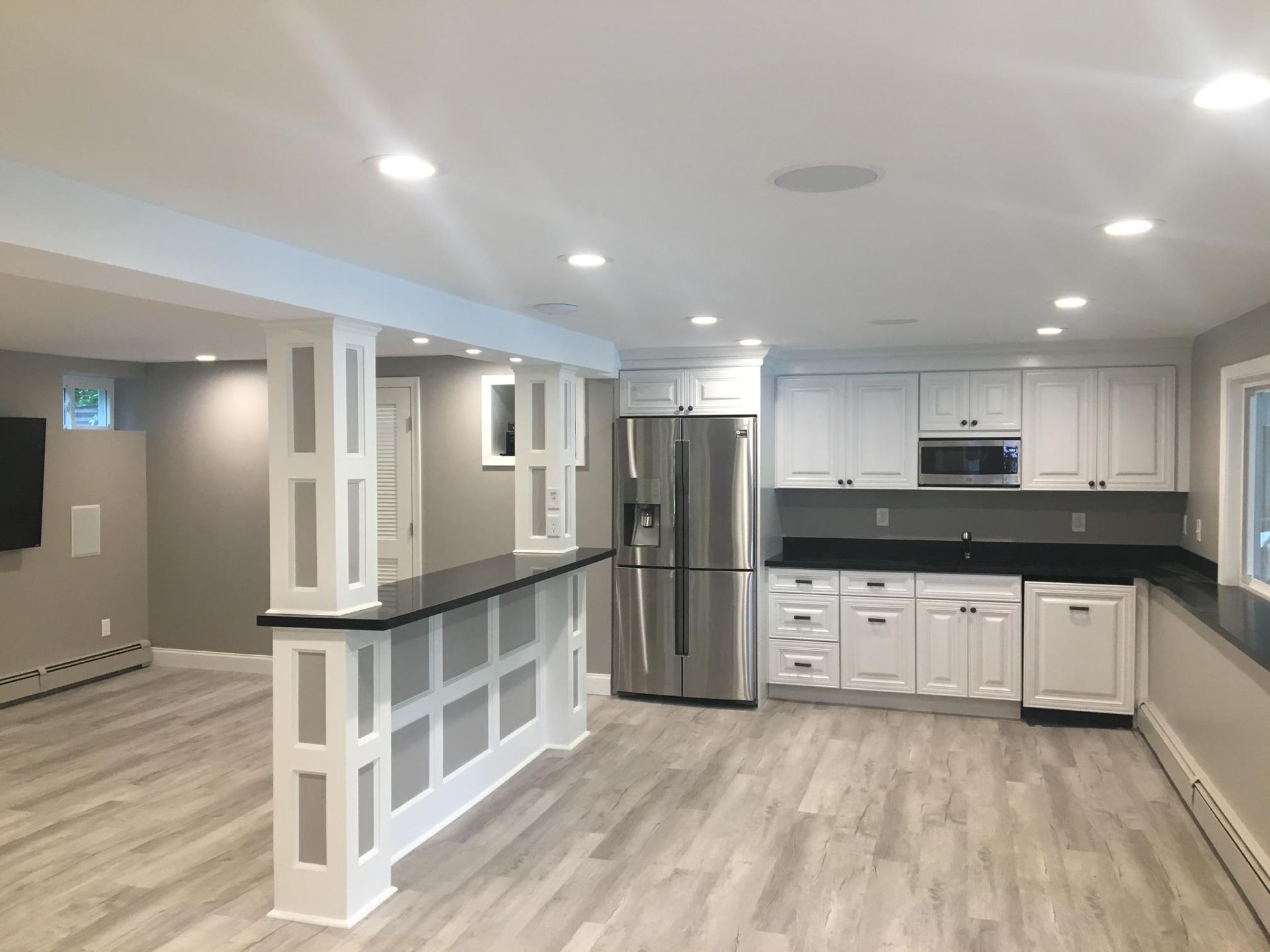 Modern kitchen with white cabinets, stainless steel fridge, and gray flooring; counter bar.