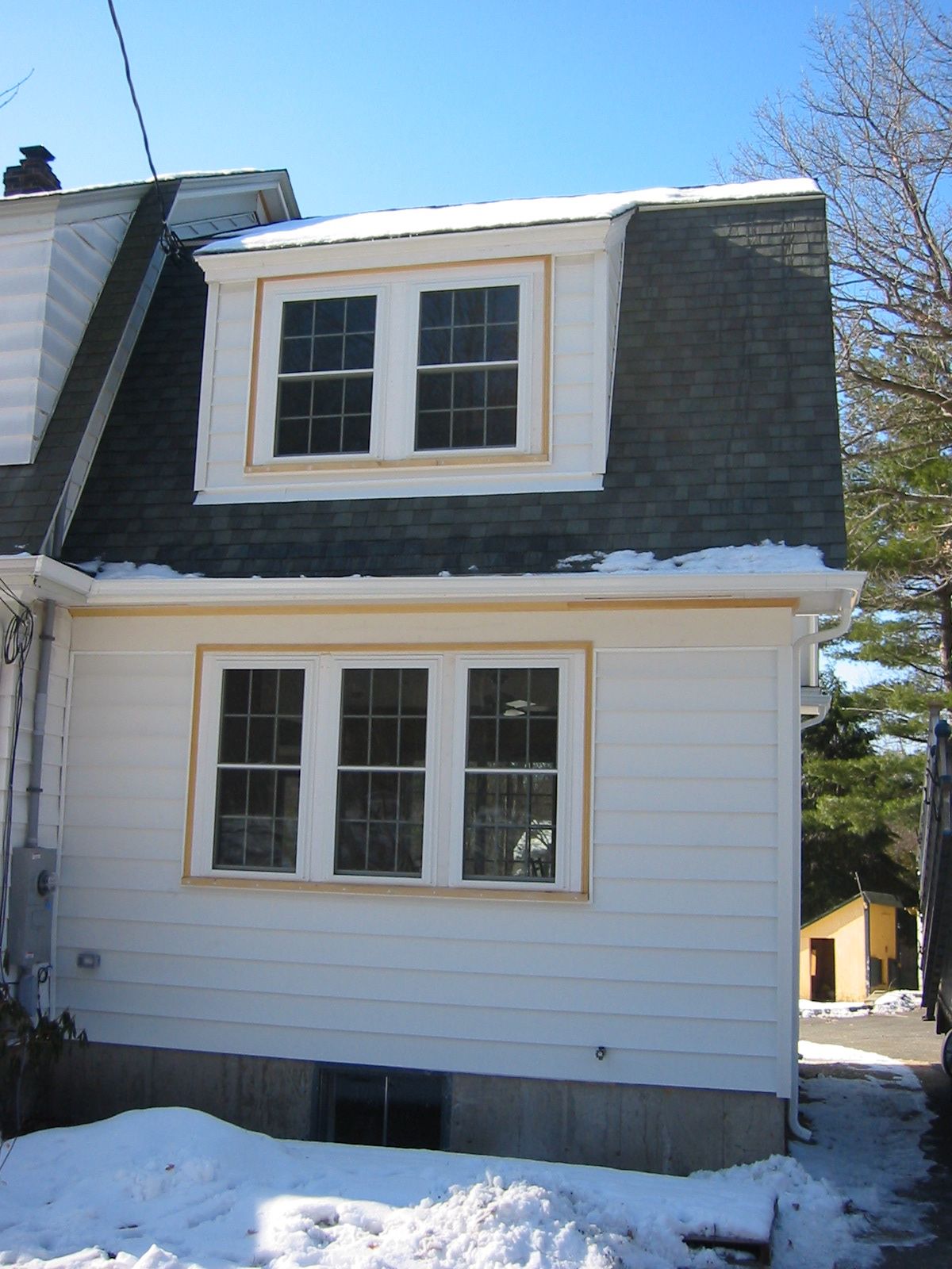 Side view of a white house with windows, a snow-covered ground, and a blue sky.