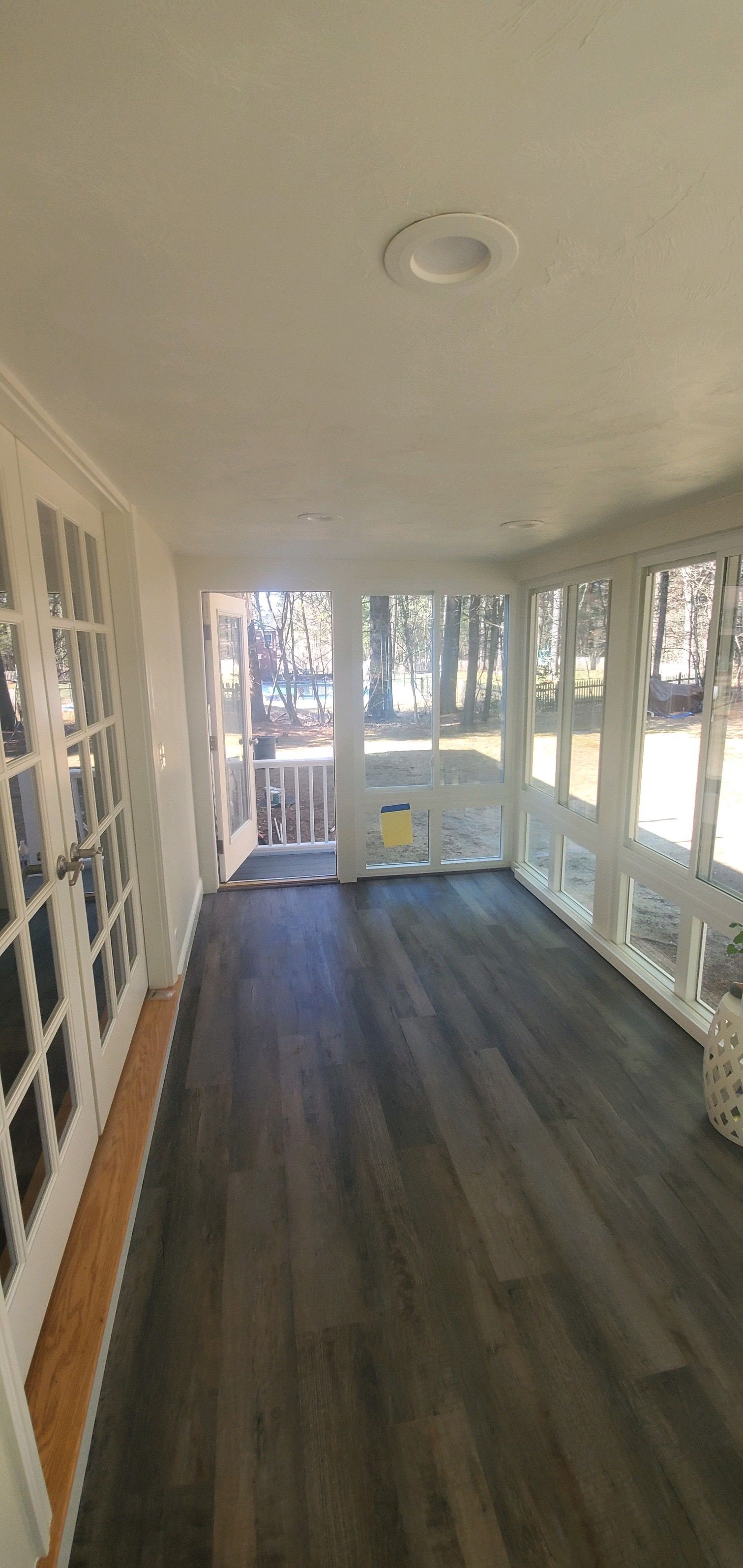 Sunroom with gray wood-look flooring, white trim, and windows. Light shines in from the outside.