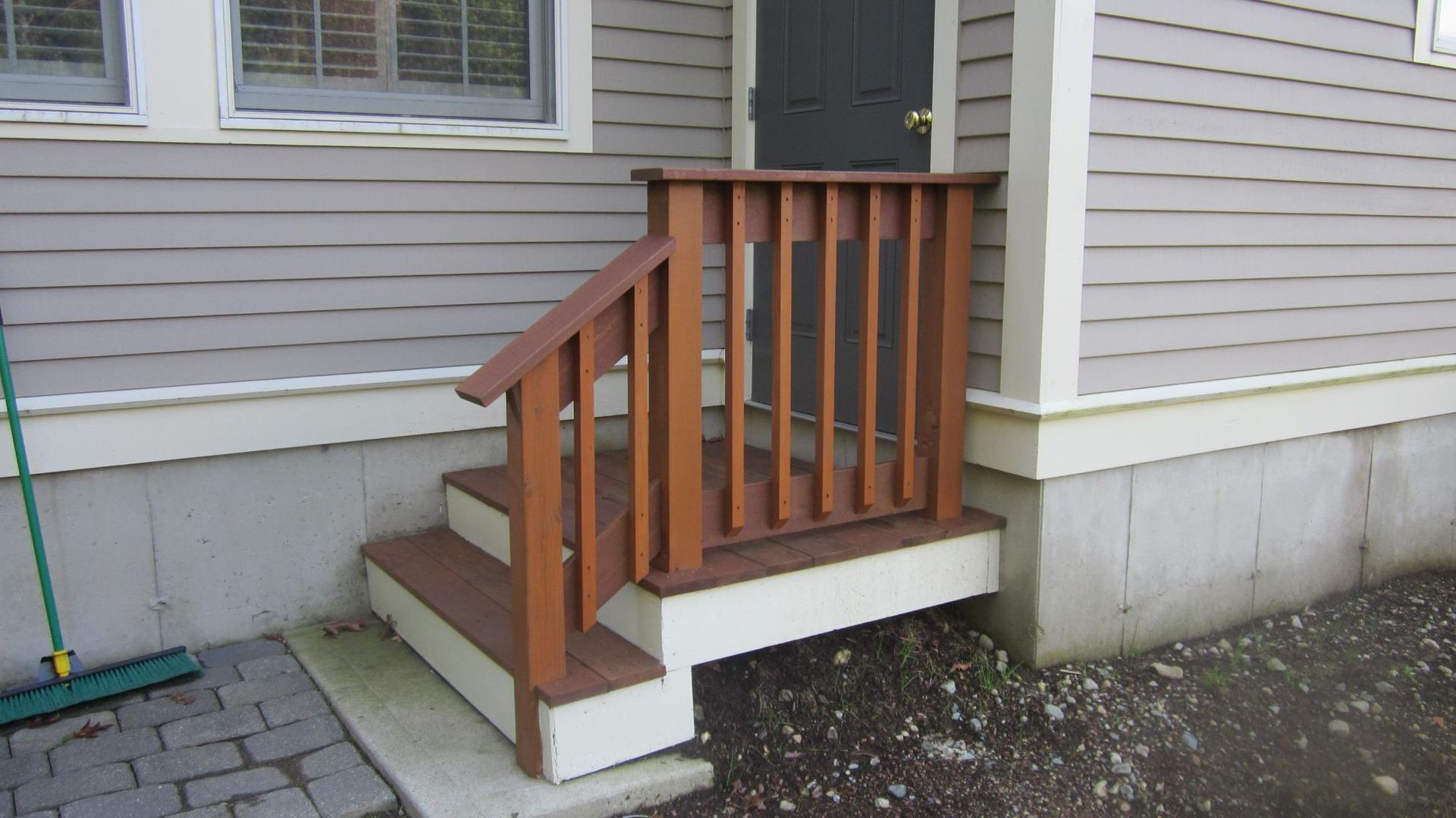 Wooden steps with handrail leading to a gray door on a light-gray house.