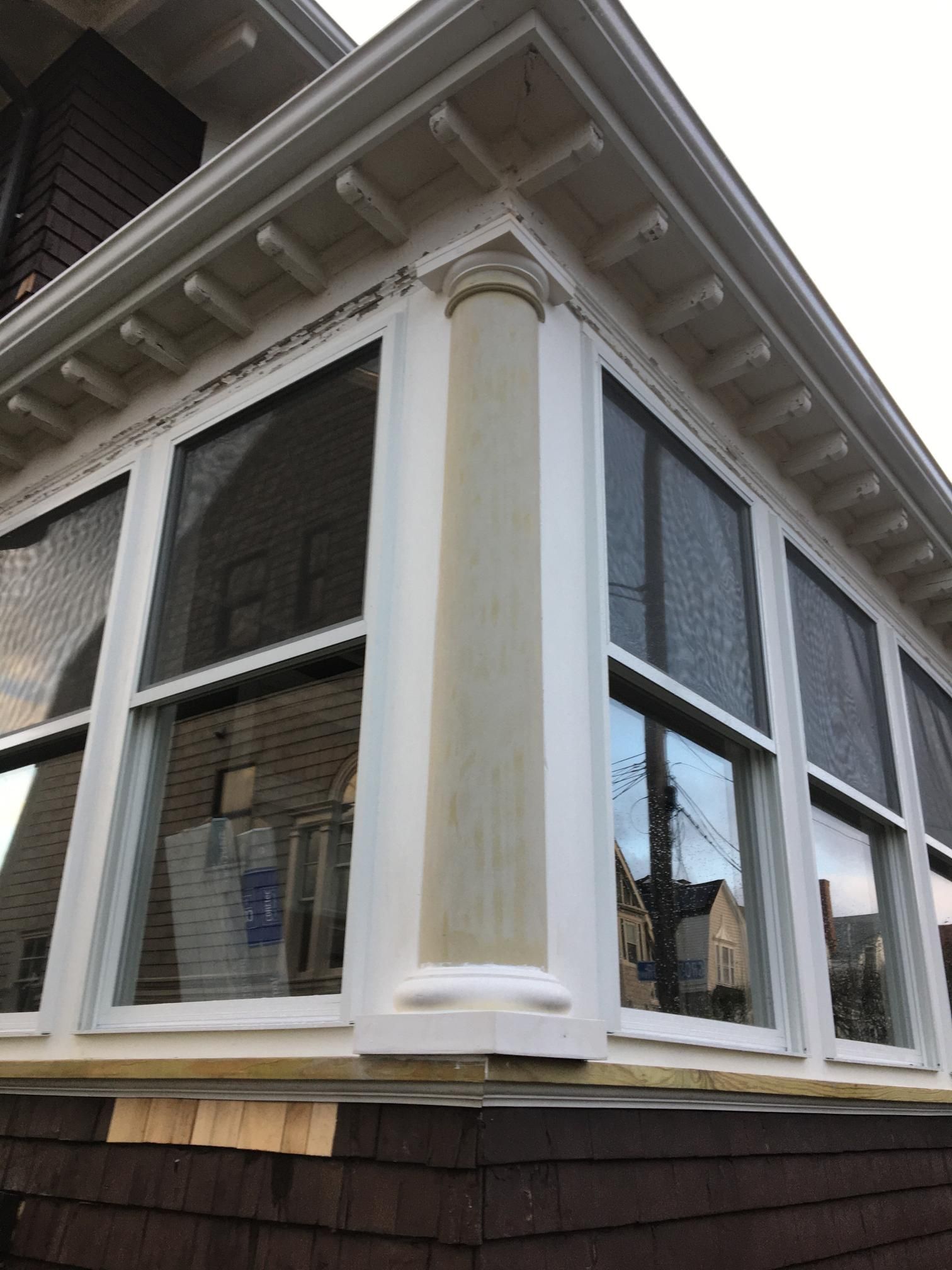 Corner of a house with white windows, decorative column, and brown siding.