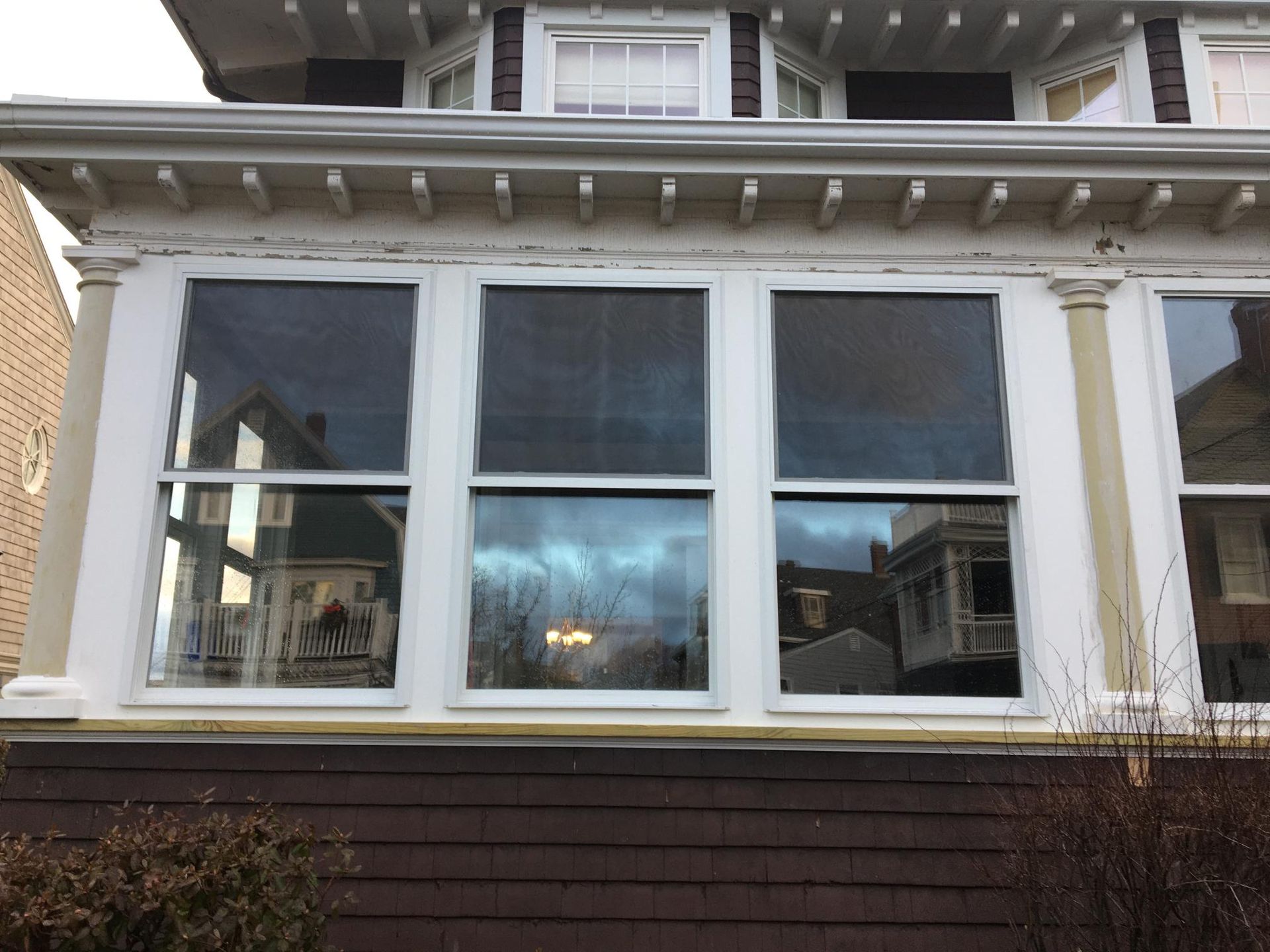 Front of a house with white framed windows, dark brown siding, and architectural details.