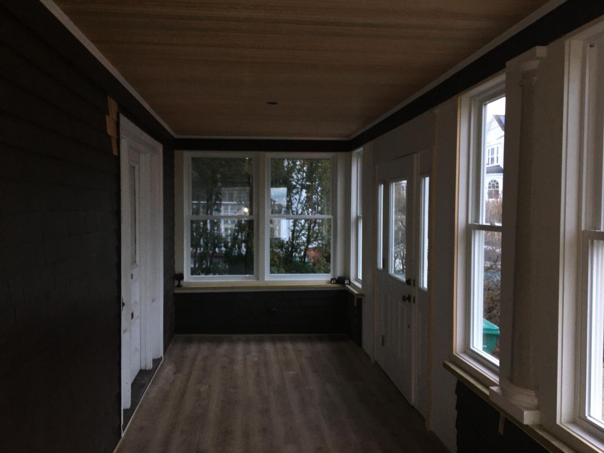 Enclosed porch with windows, door, wood floor, and dark-colored walls and trim.