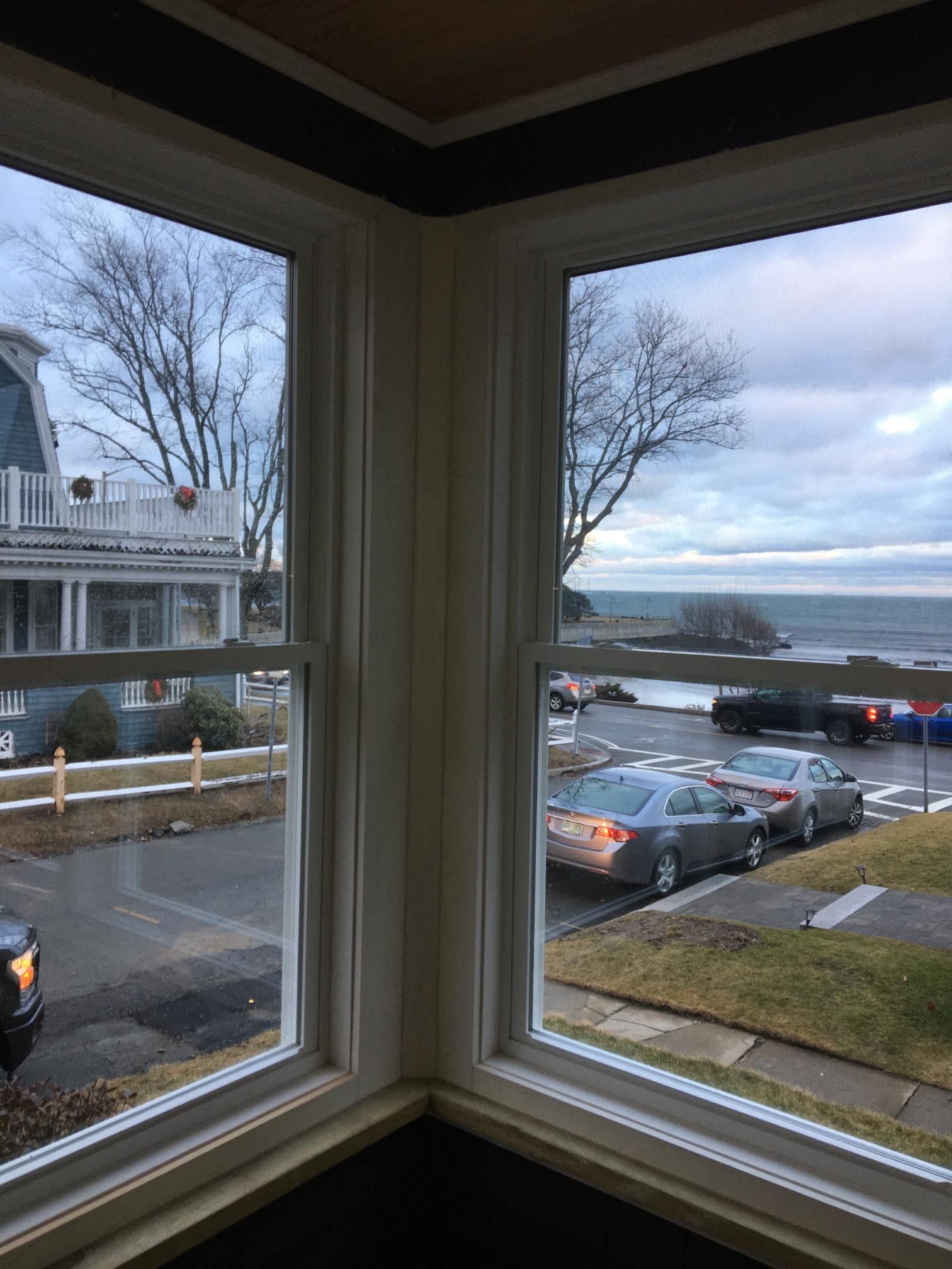 View through corner windows of street, houses, ocean, and overcast sky.