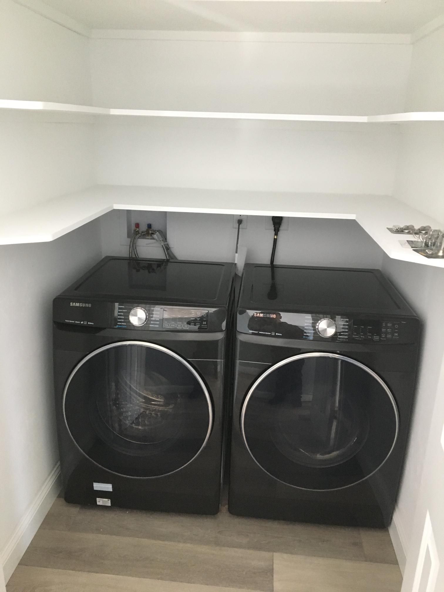 Black washer and dryer set in a laundry closet with white shelving.