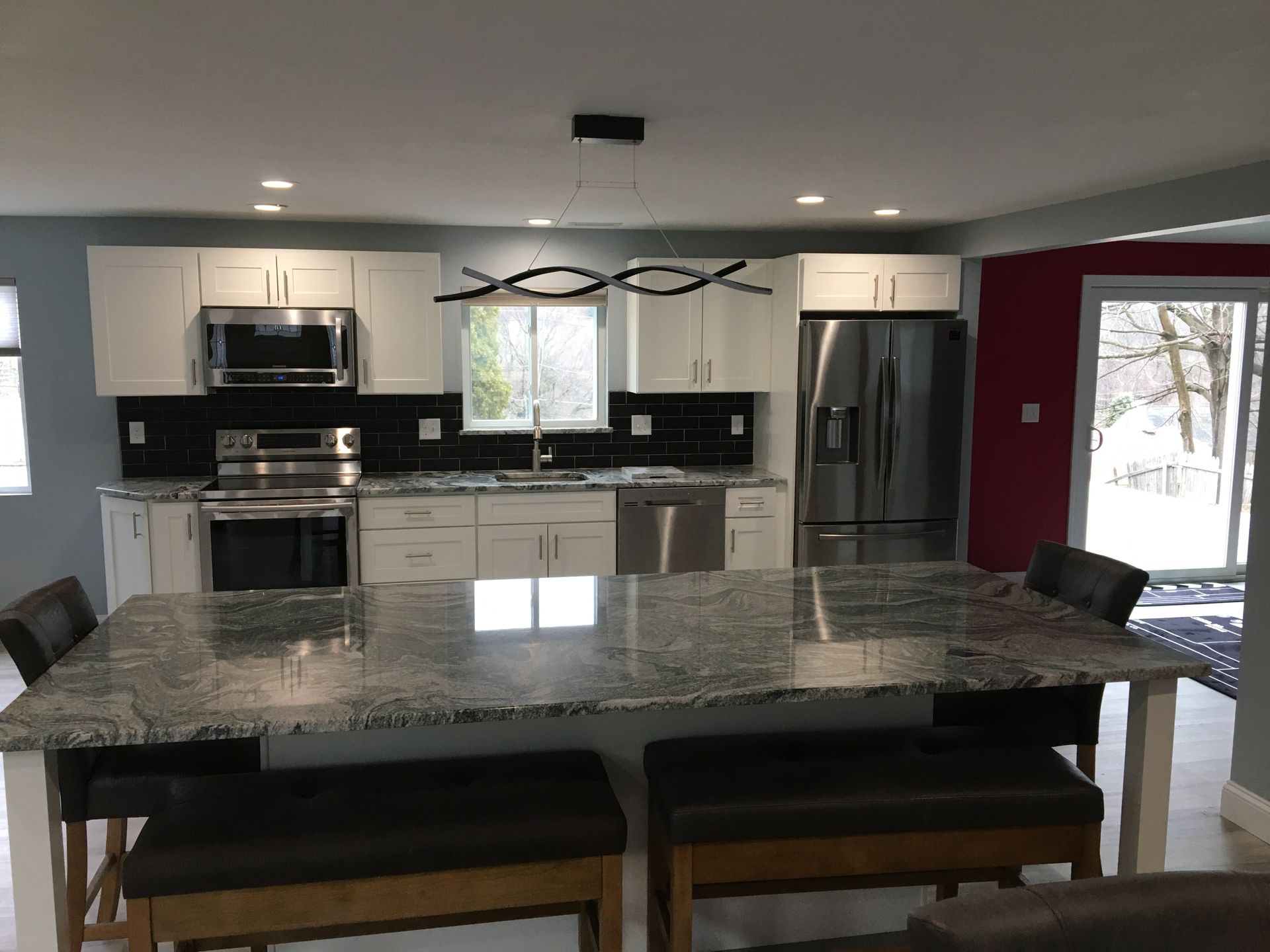 Modern kitchen with white cabinets, stainless steel appliances, granite island, and dark leather benches.