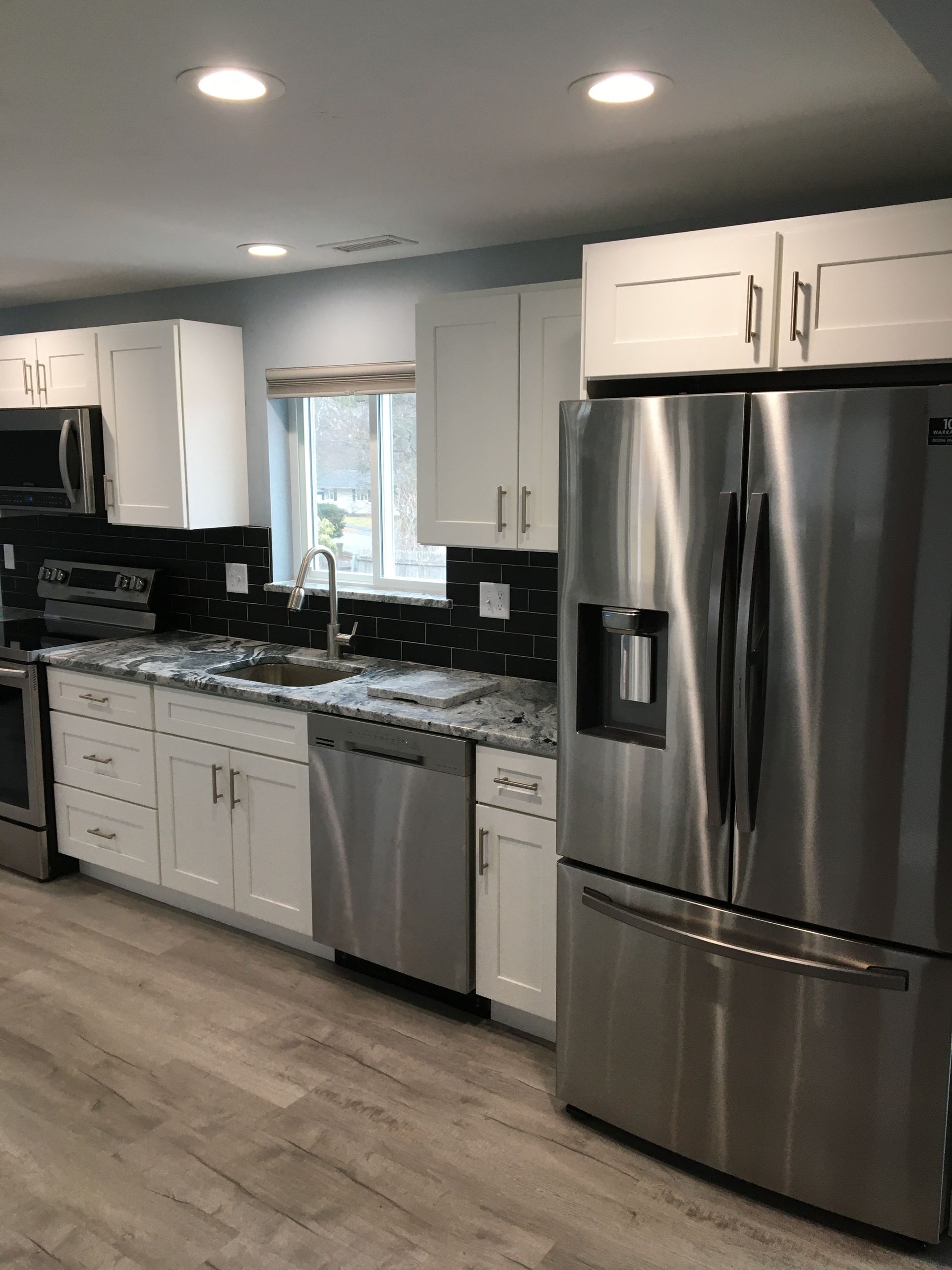 Modern kitchen with white cabinets, stainless steel appliances, and a dark backsplash.