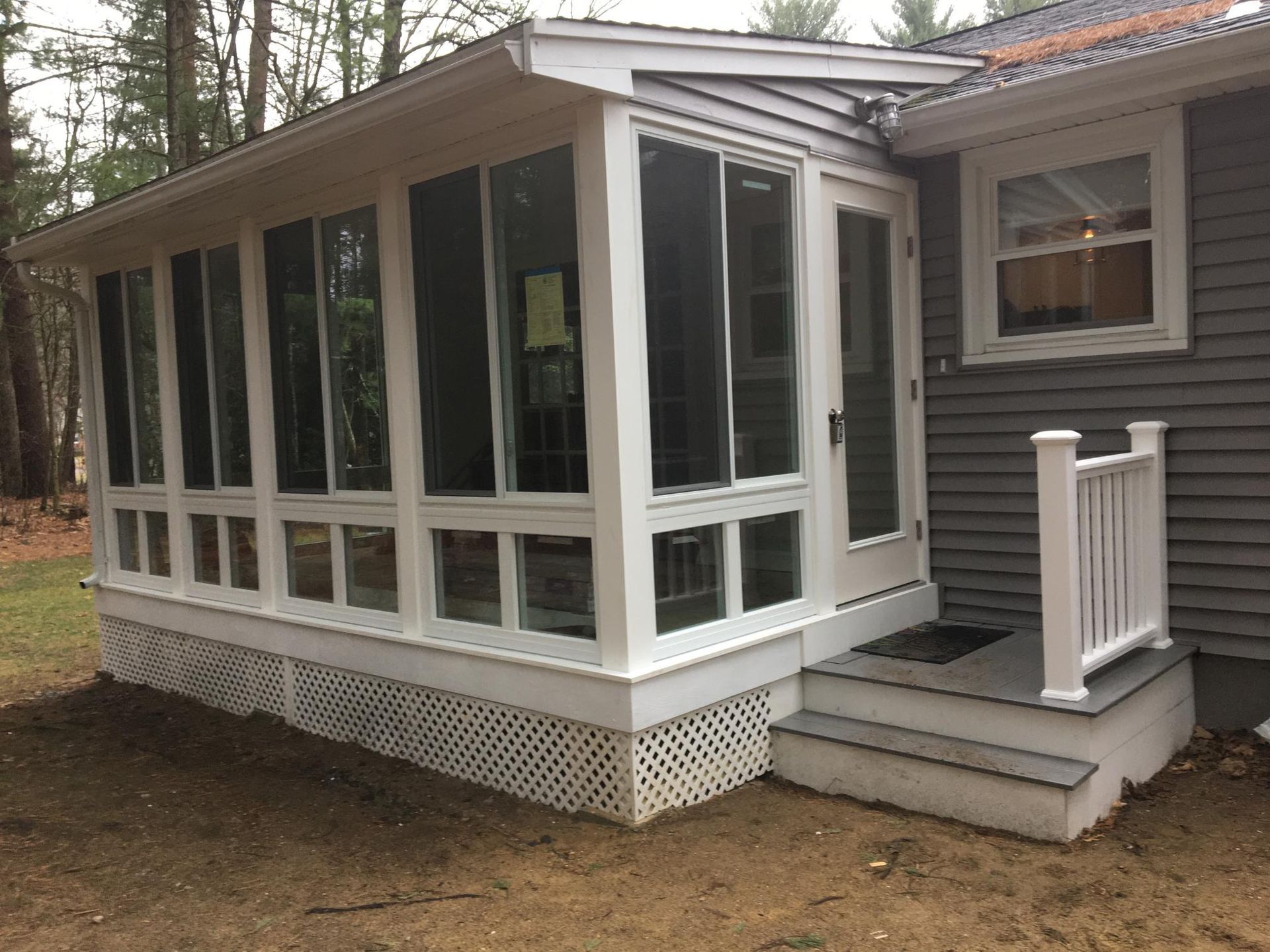 Screened porch with white trim and stairs attached to a gray house.