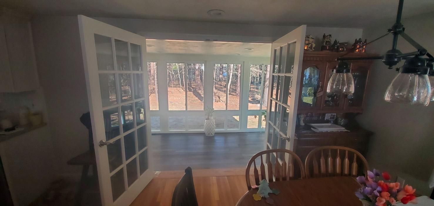 French doors open to a sunroom with trees. A dining table and chairs are in the foreground.