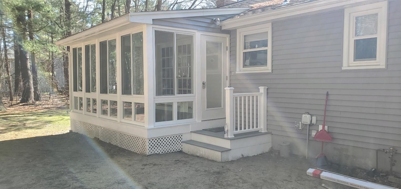 Screened porch attached to a gray house, set in a yard with trees.