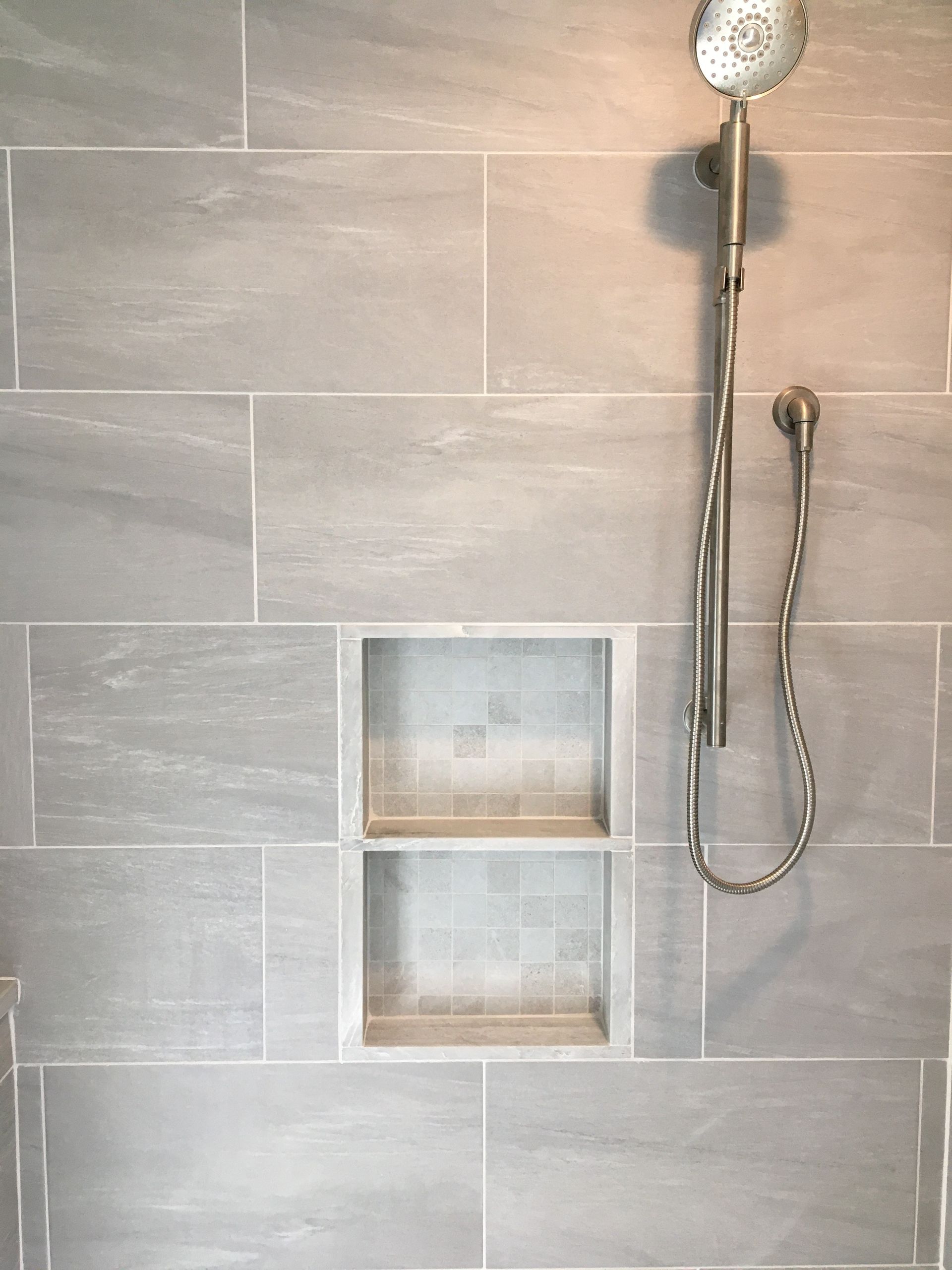 Gray tiled shower with built-in shelves and a handheld showerhead.