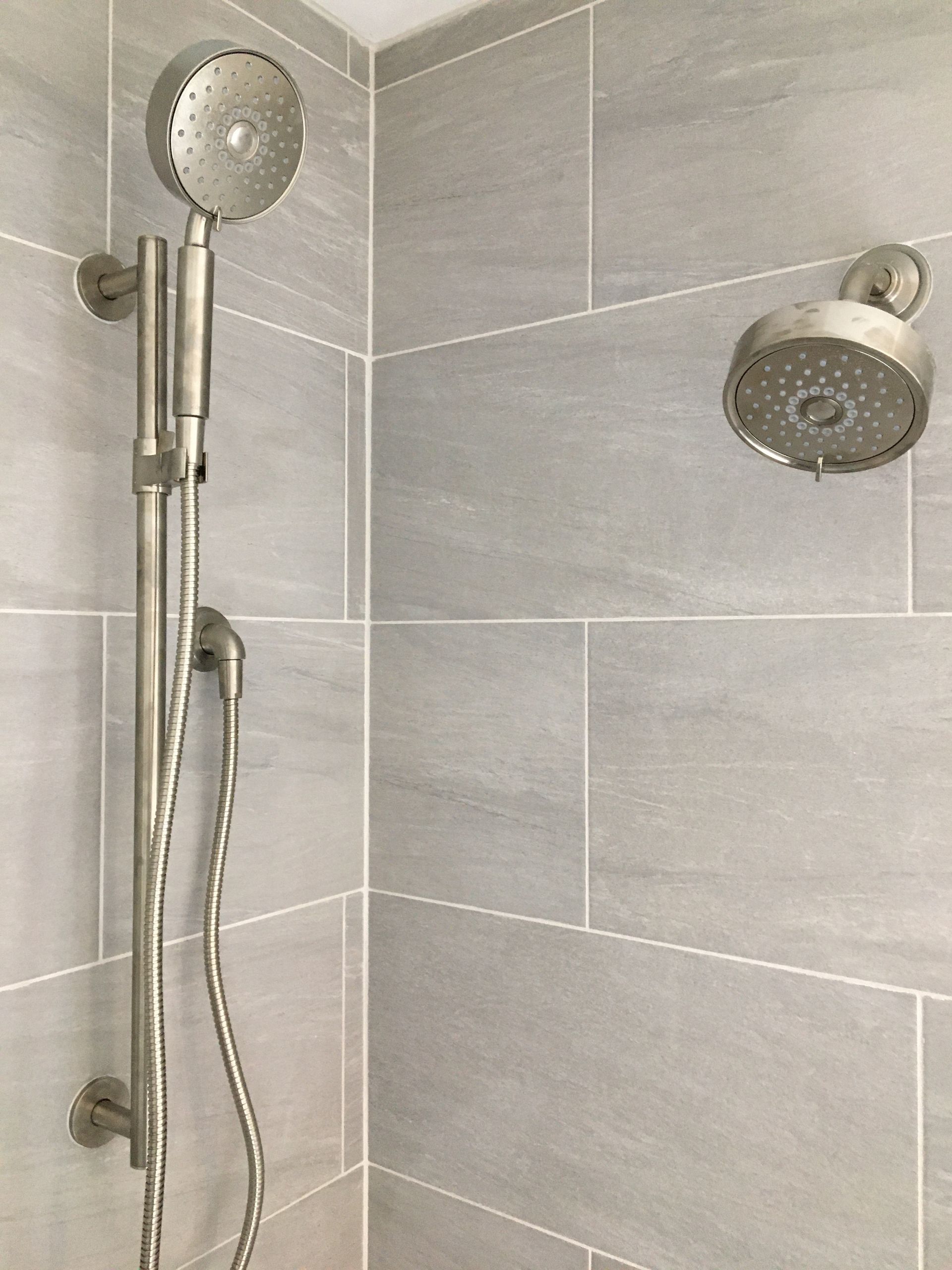 Shower stall with gray tiled walls and two silver showerheads.