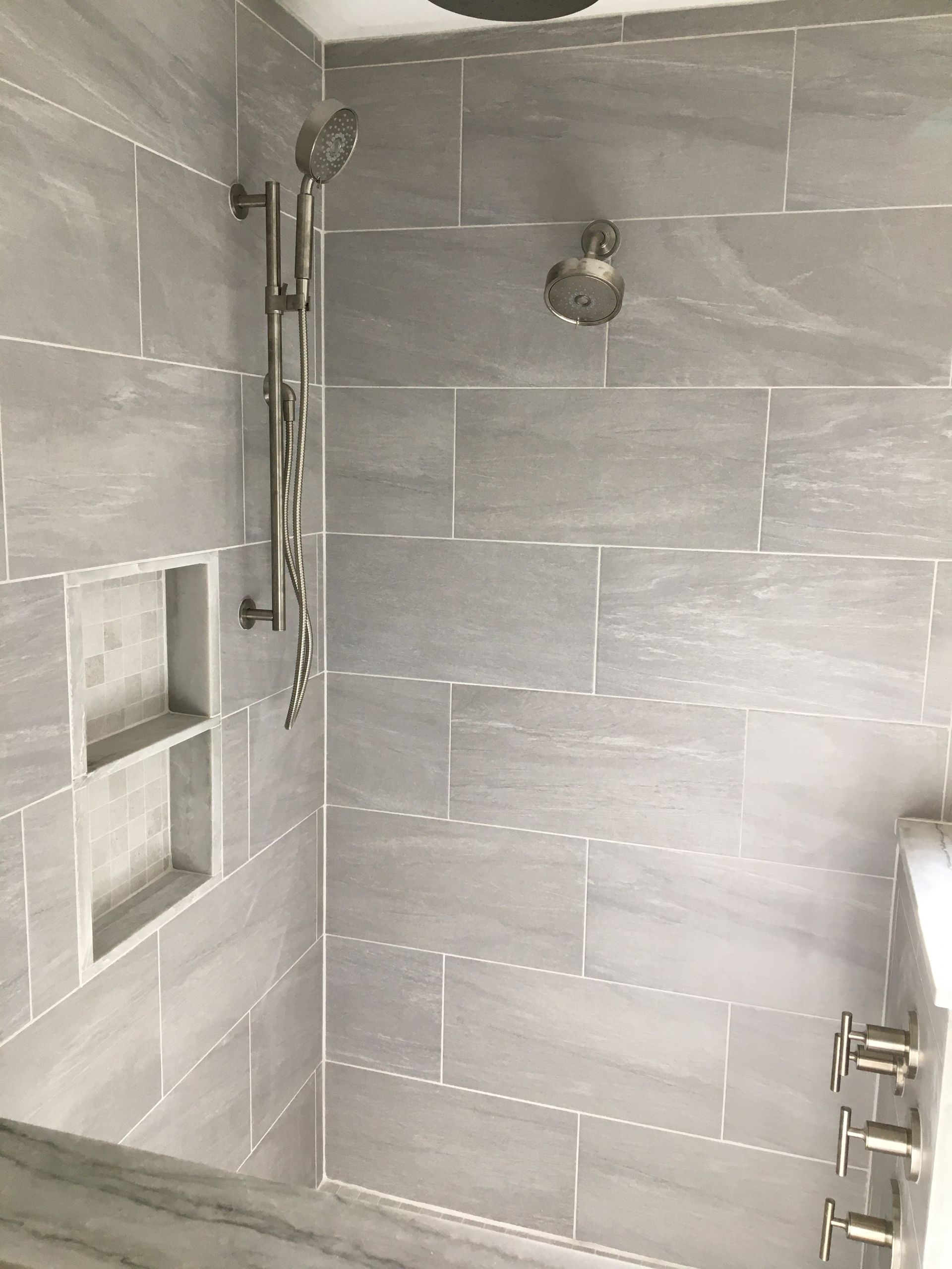 Gray tile shower with silver fixtures, a built-in shelf, and two shower heads.