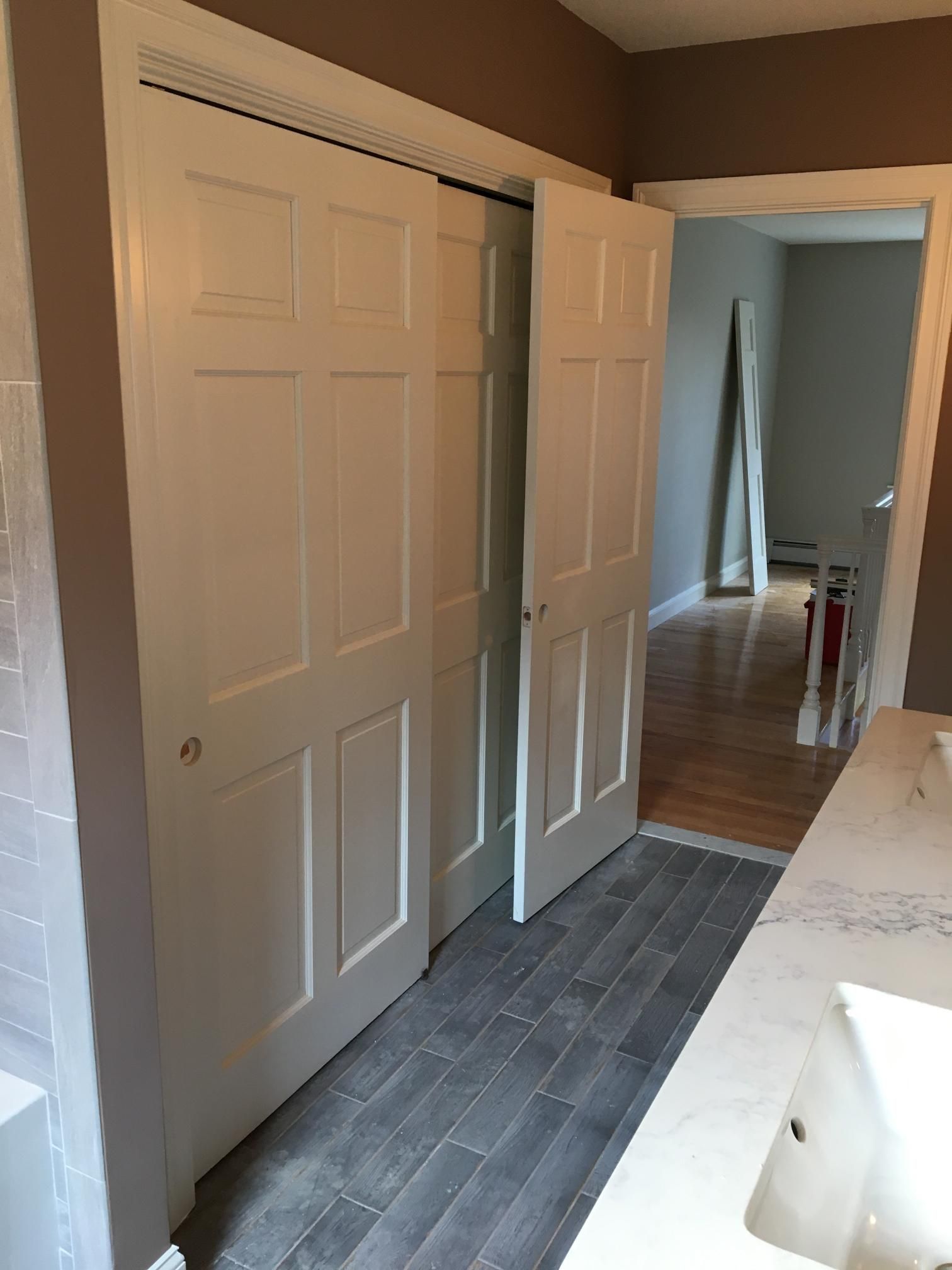 White sliding closet doors in a bathroom, one open, with a view of a hallway.
