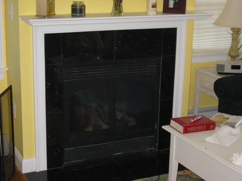 Black tiled fireplace with white mantel and yellow wall.