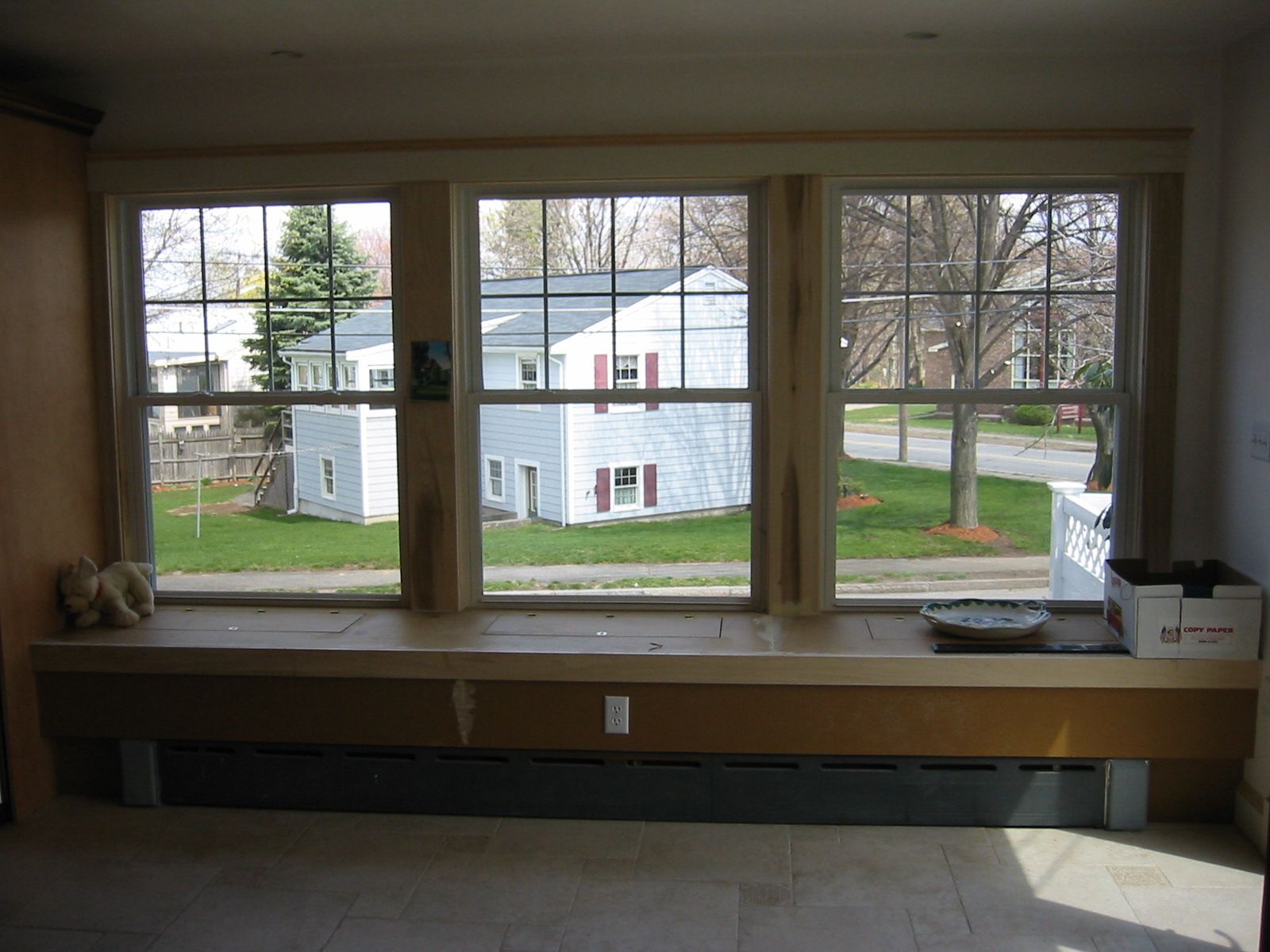 Triple window with a built-in bench overlooking a residential street with houses and grass.