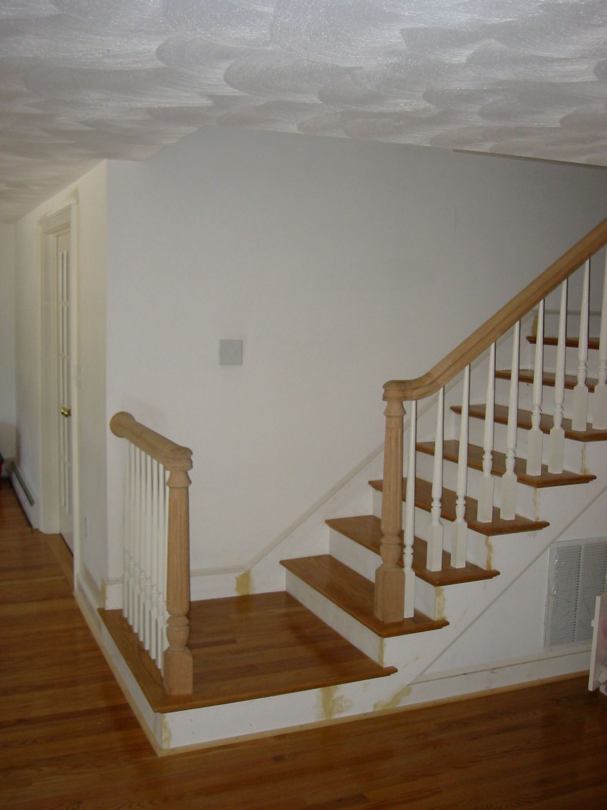 Staircase with wooden steps and white balustrade in a room with hardwood floors and a door.