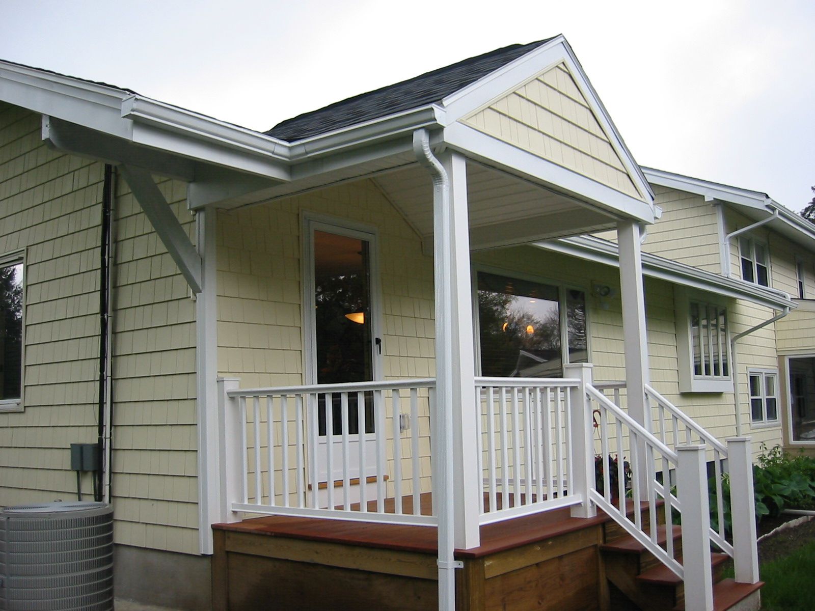 Yellow house with a white porch, railing, and roof trim. Brown wooden deck and steps.