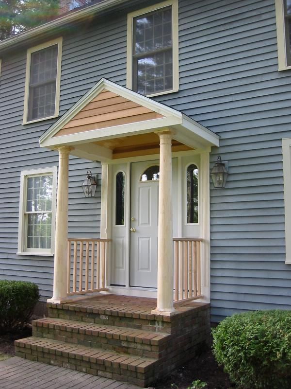 Blue house with white door and small portico, brick steps, and bushes.