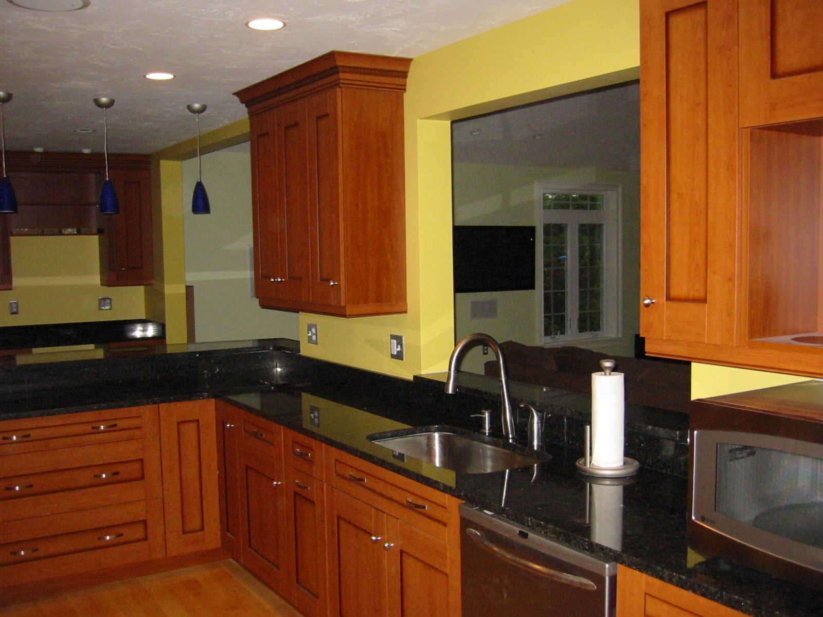 Kitchen with wooden cabinets, black countertops, and yellow walls; stainless steel sink and appliances.