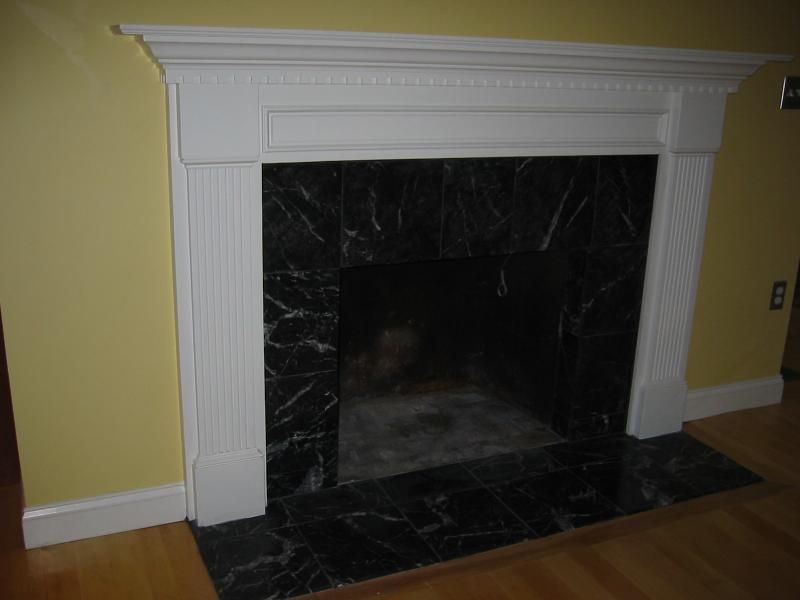 White fireplace with black marble interior and surround, in a room with yellow walls and wood floor.