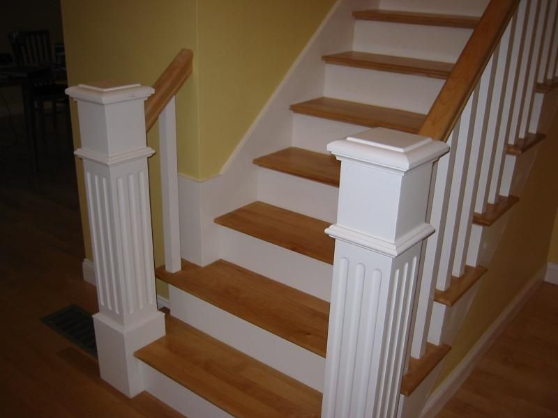 Wooden staircase with white columns, wooden steps and banister, yellow wall.