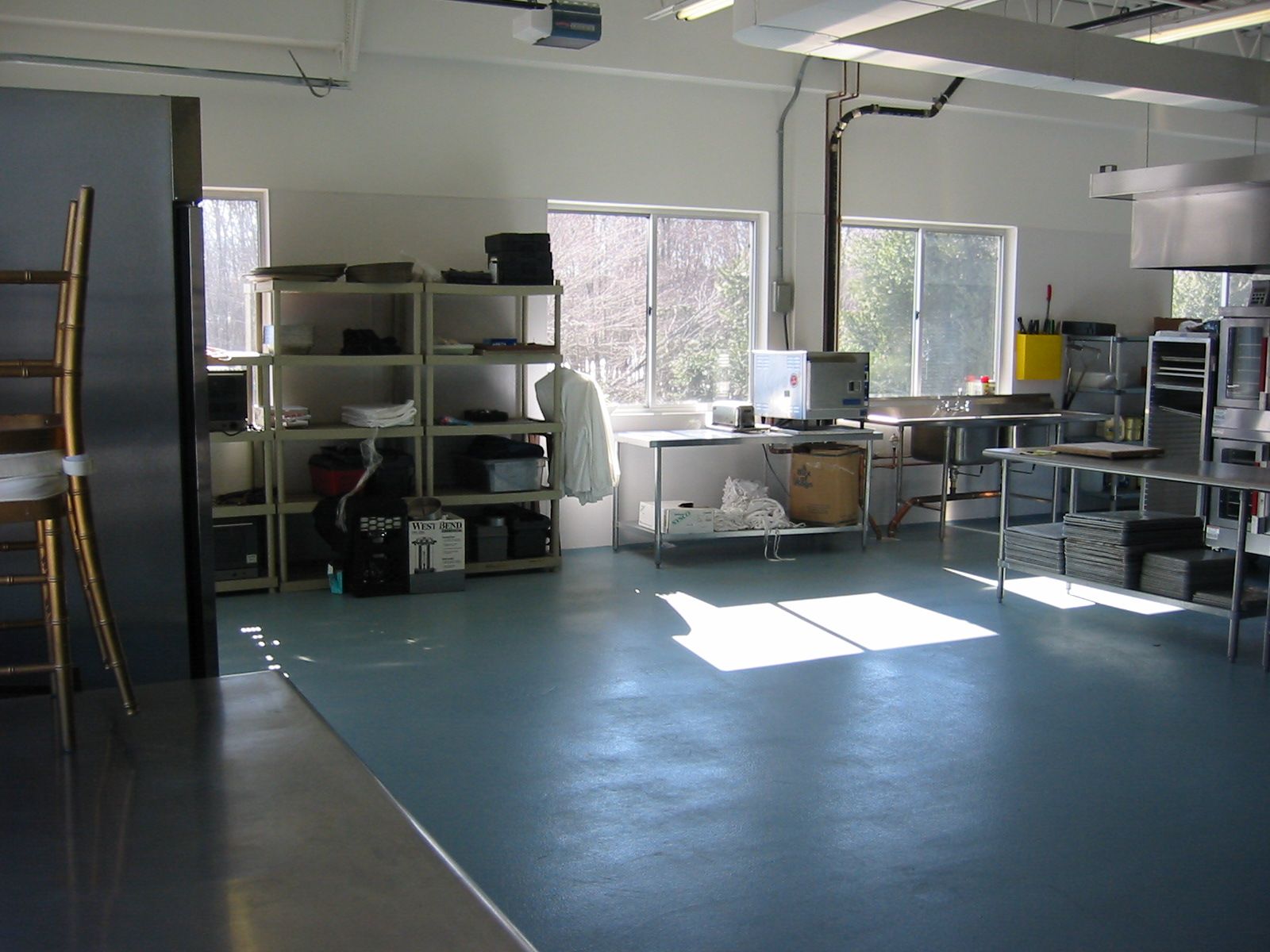 A light-filled workshop with blue floor, metal shelves holding electronics, and a large window.