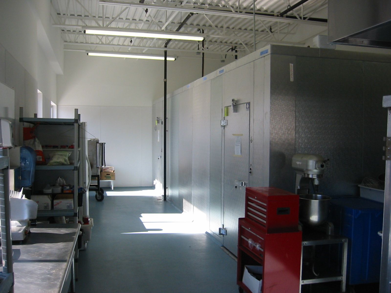 A commercial kitchen interior with a walk-in cooler, work stations, and a light blue floor.