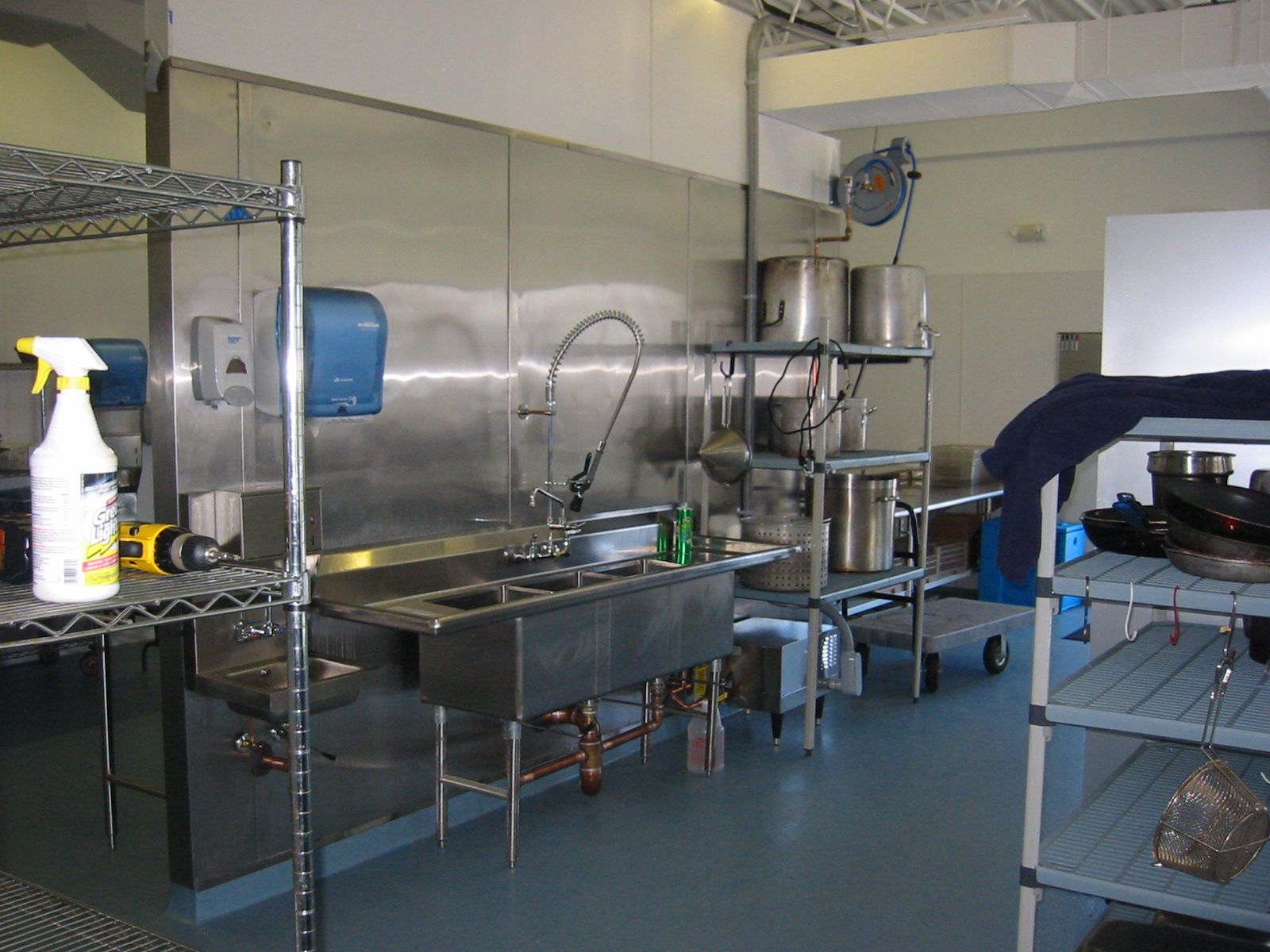 Commercial kitchen with stainless steel sinks, shelving, and equipment.