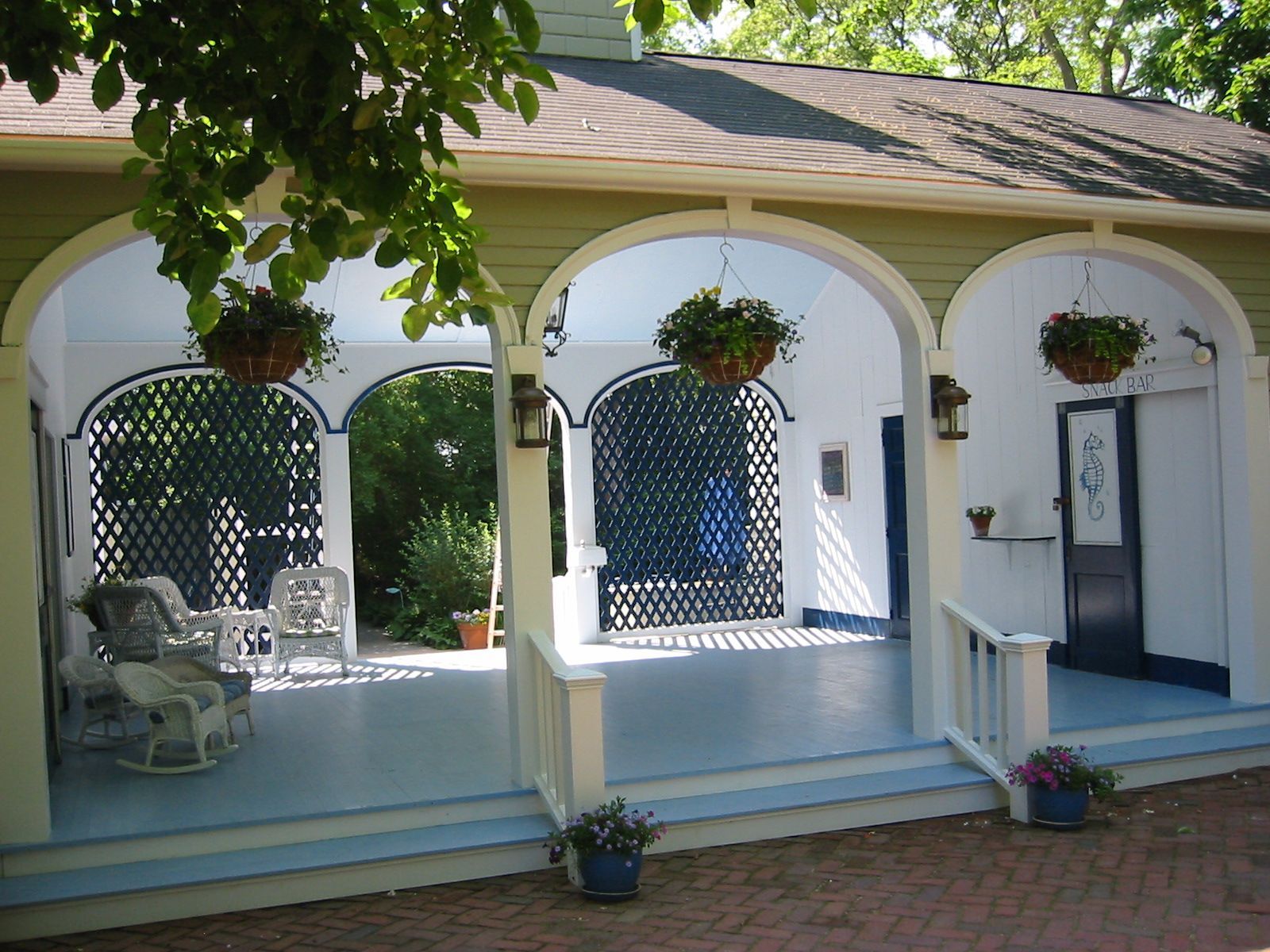 Covered porch with arches, hanging baskets, and lattice screens. White and blue color scheme, brick patio.