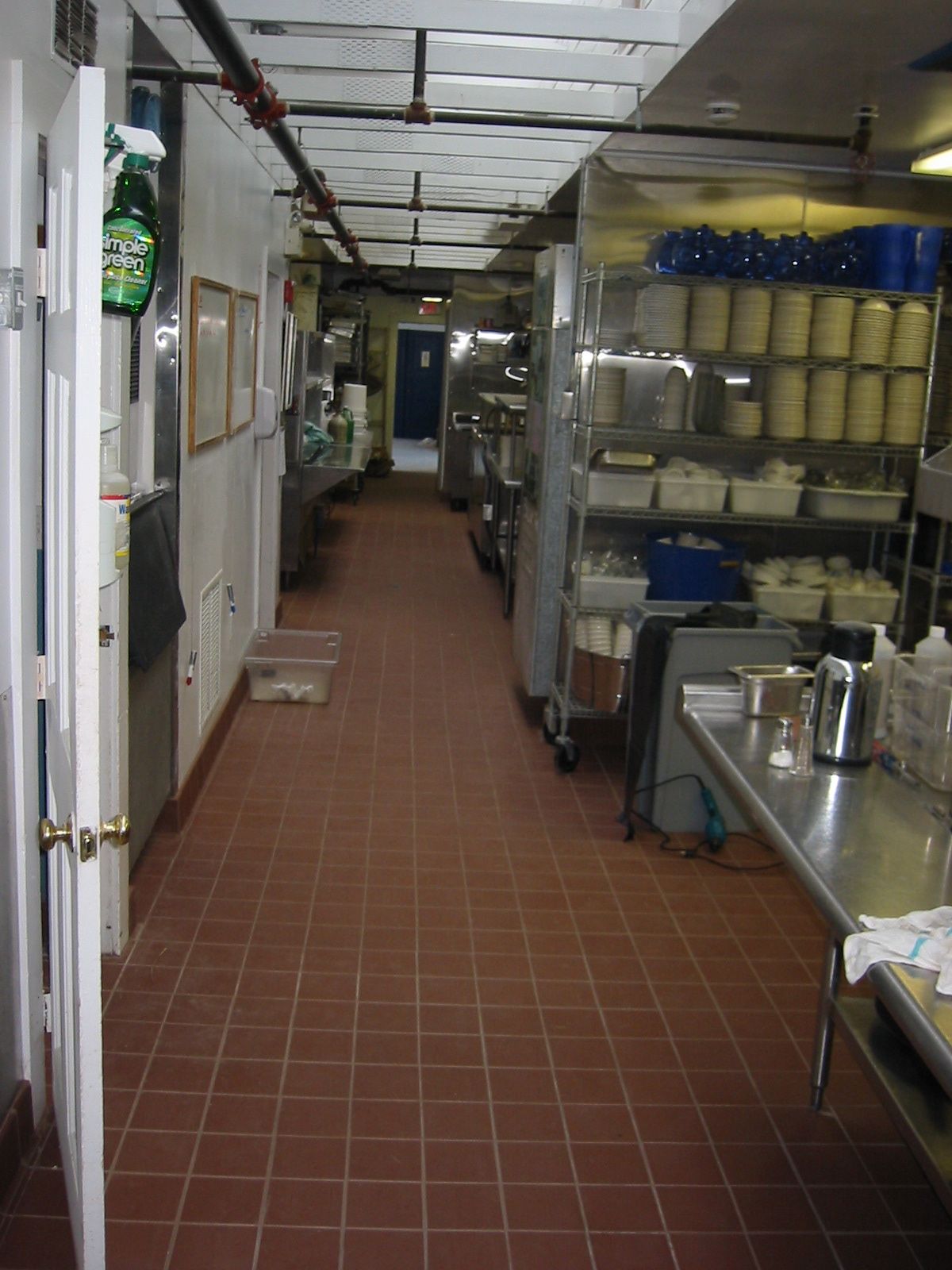 Narrow commercial kitchen hallway with red tiled floor and metal countertops.