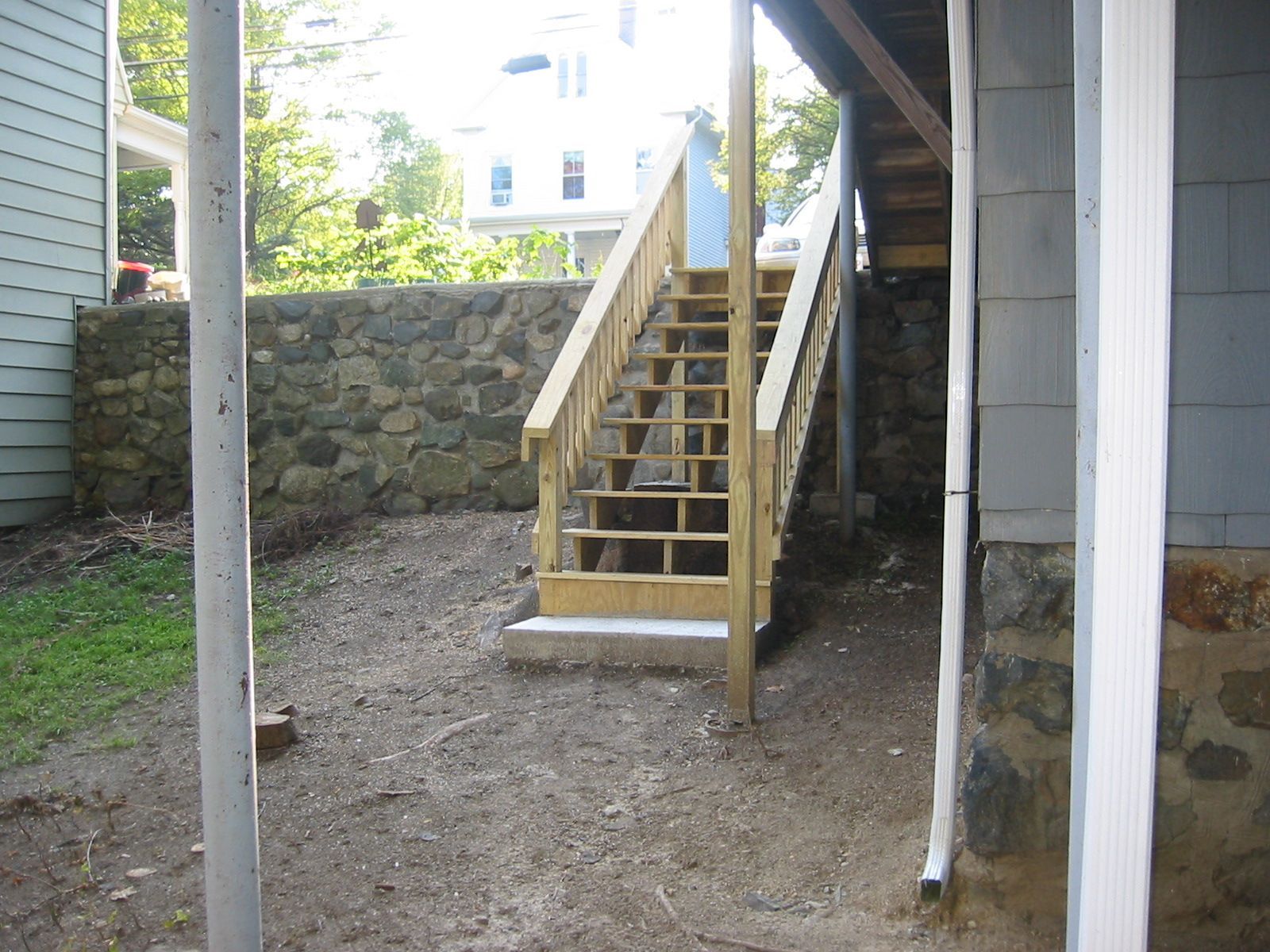 Wooden staircase leading up from a gravel path, next to a stone wall and a house.