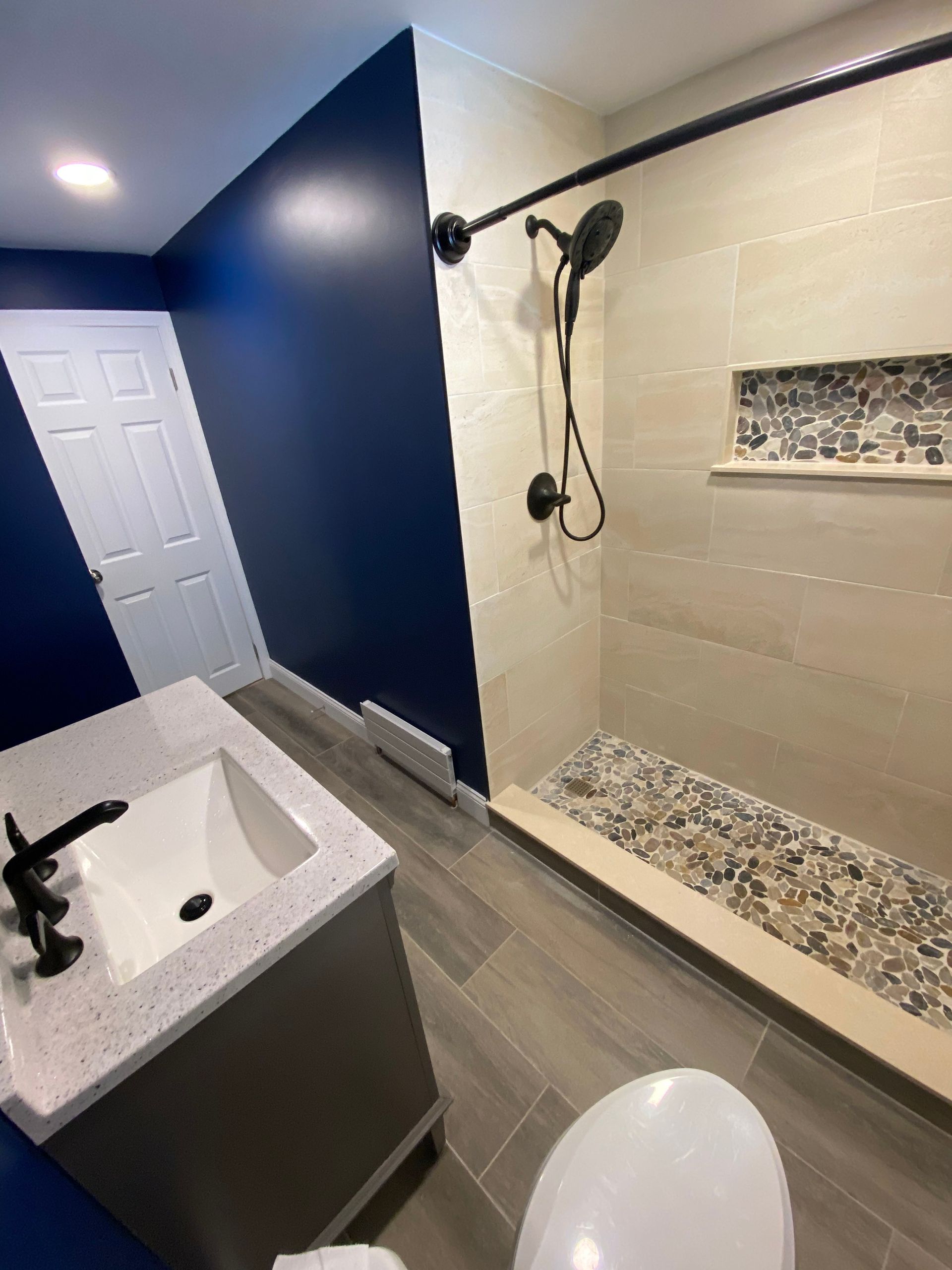 Modern bathroom with dark blue walls, shower, vanity, and toilet.