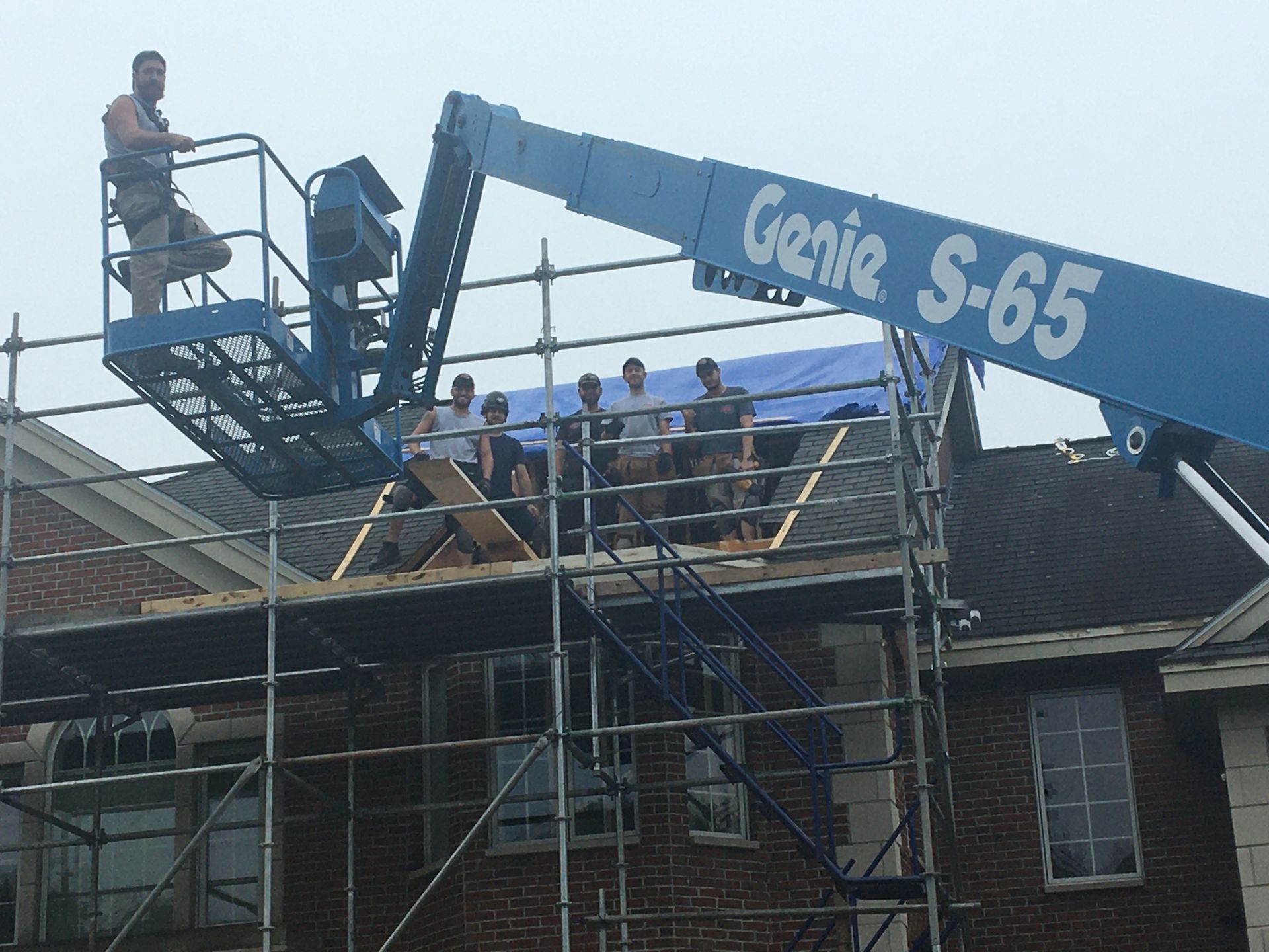 Construction workers on roof, using scaffolding and a lift to work on the roof of a brick building.