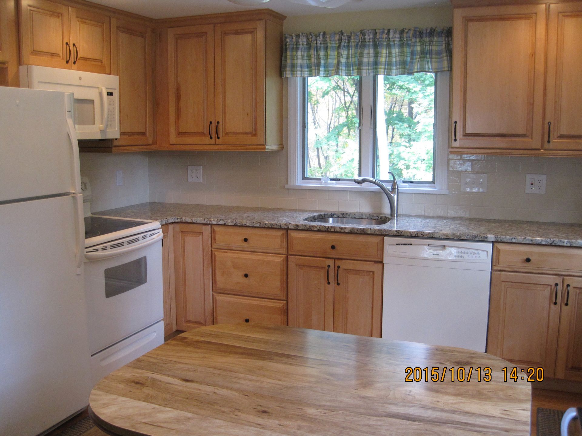 Kitchen with light wood cabinets, white appliances, and granite countertops.