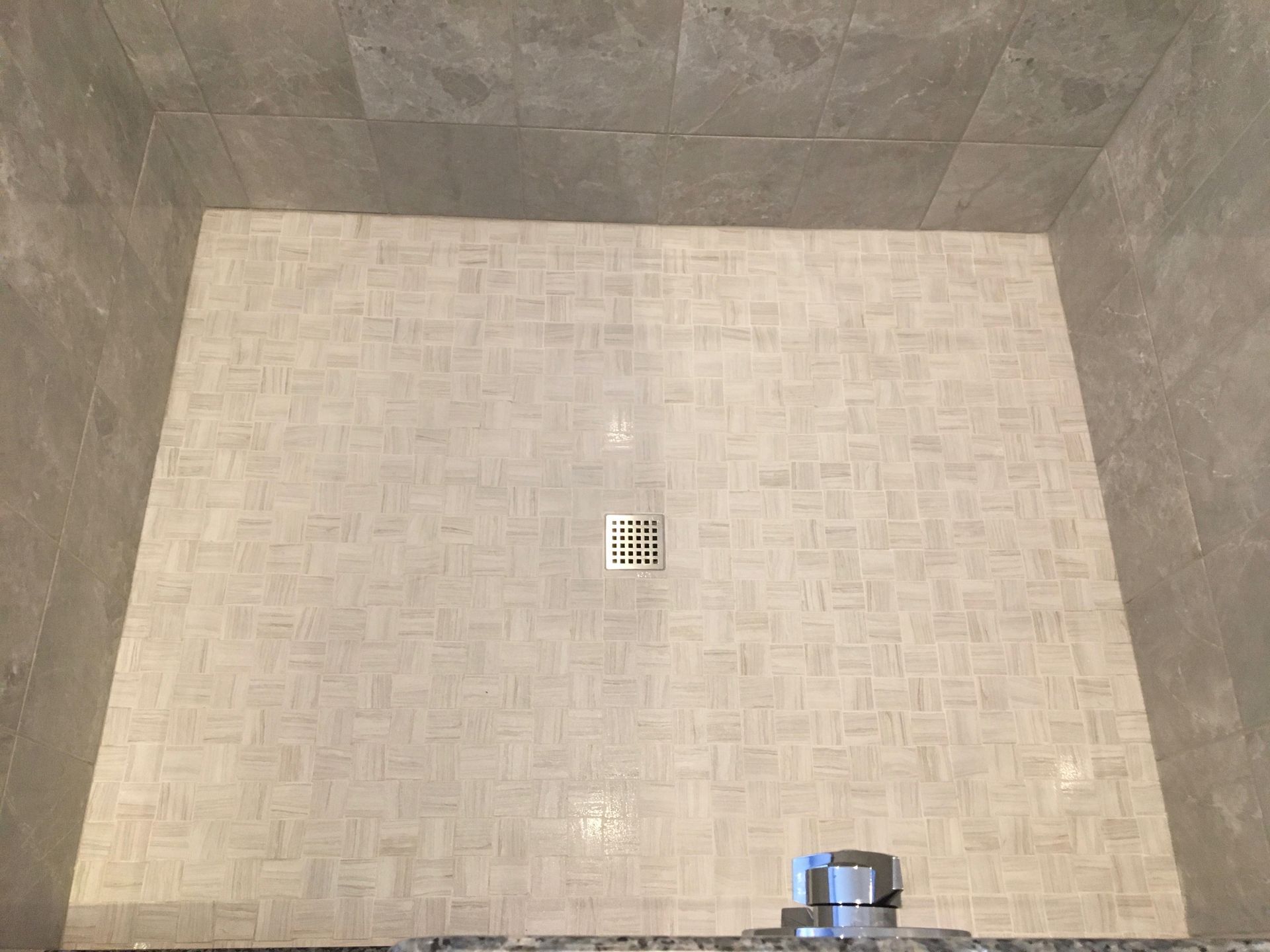 Shower with light gray tile walls and floor, a central drain, and a silver fixture at the bottom.