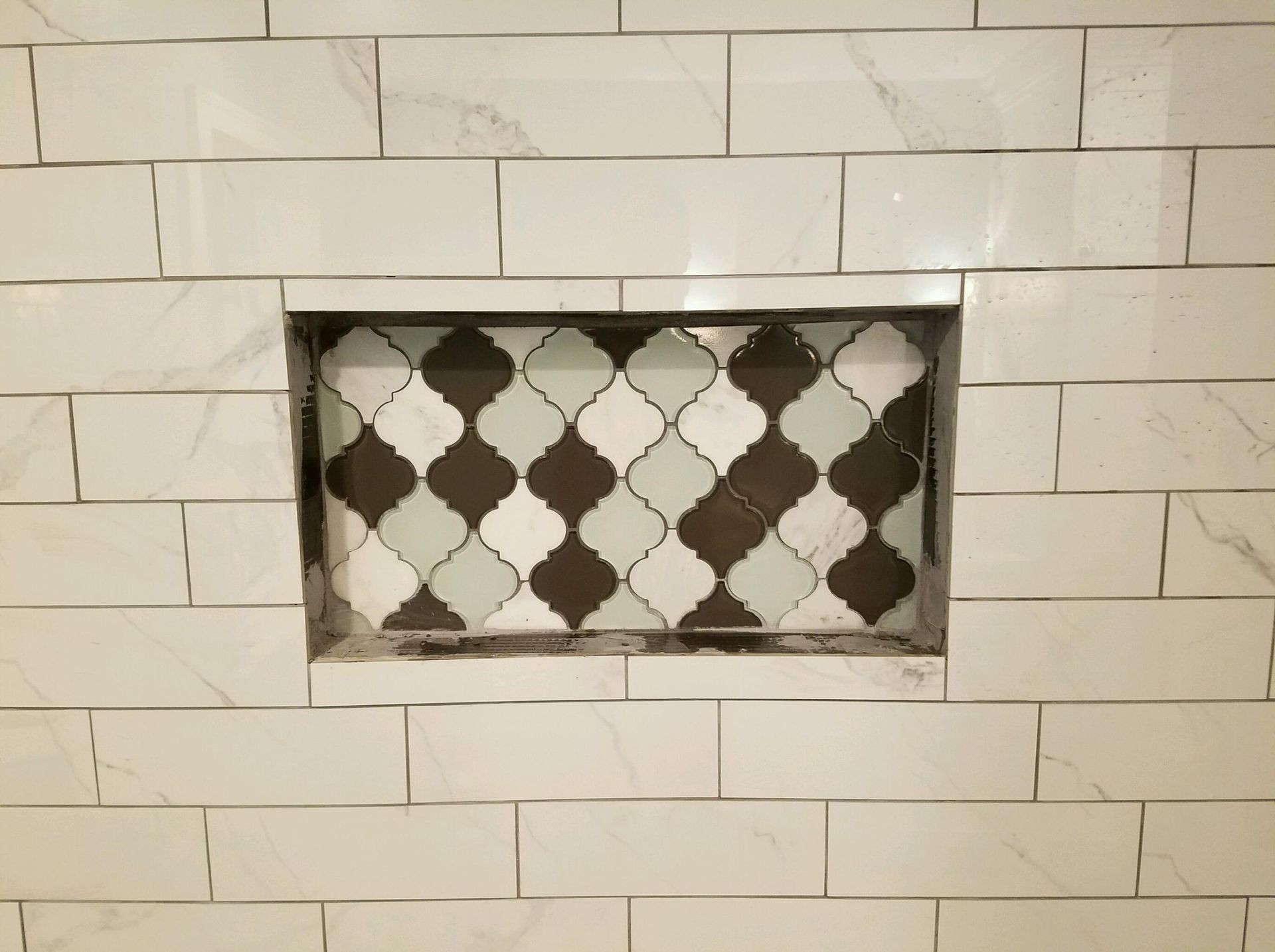 Tiled shower niche with decorative patterned tiles set within a white tiled wall.