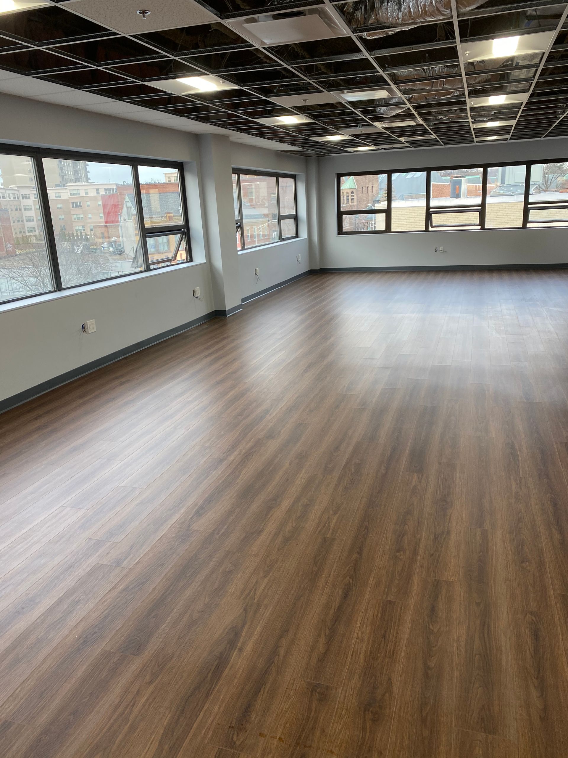 Empty room with wood-look flooring and multiple windows, dark ceiling, and white walls.