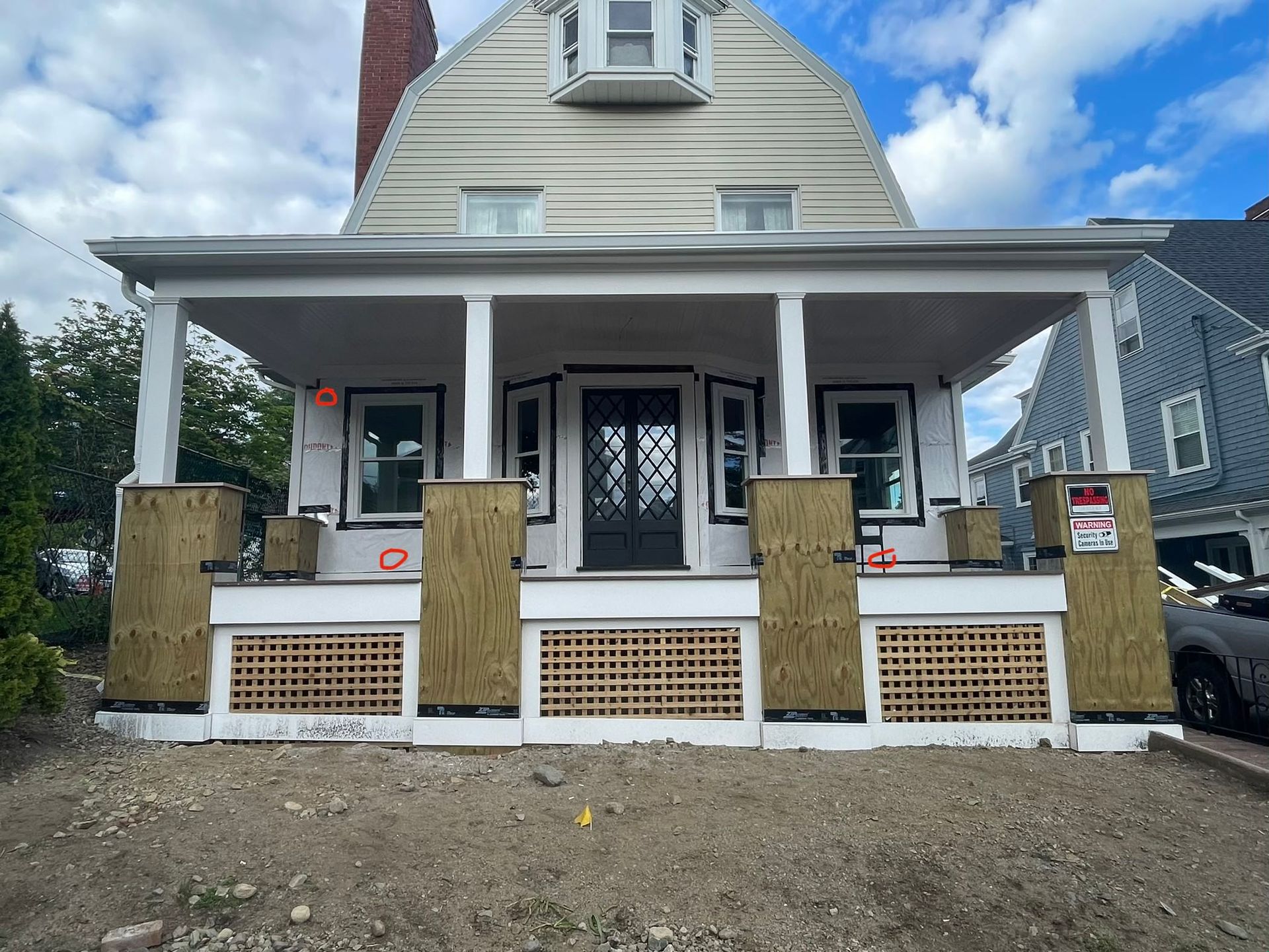House exterior with a porch under construction, featuring white columns, a black door, and lattice details.