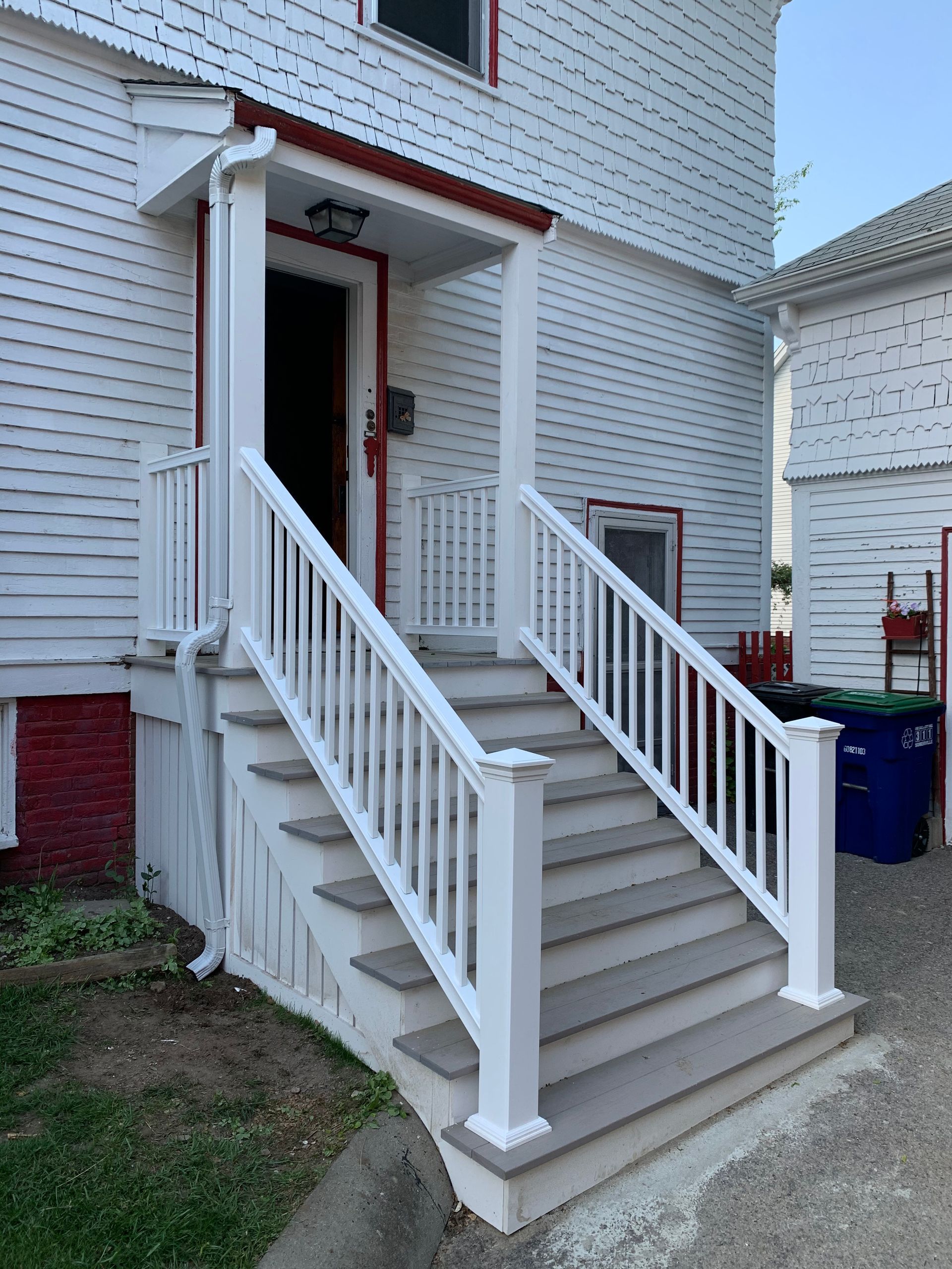 White stairs lead to a white porch with a red roof and trim on a building with white siding.