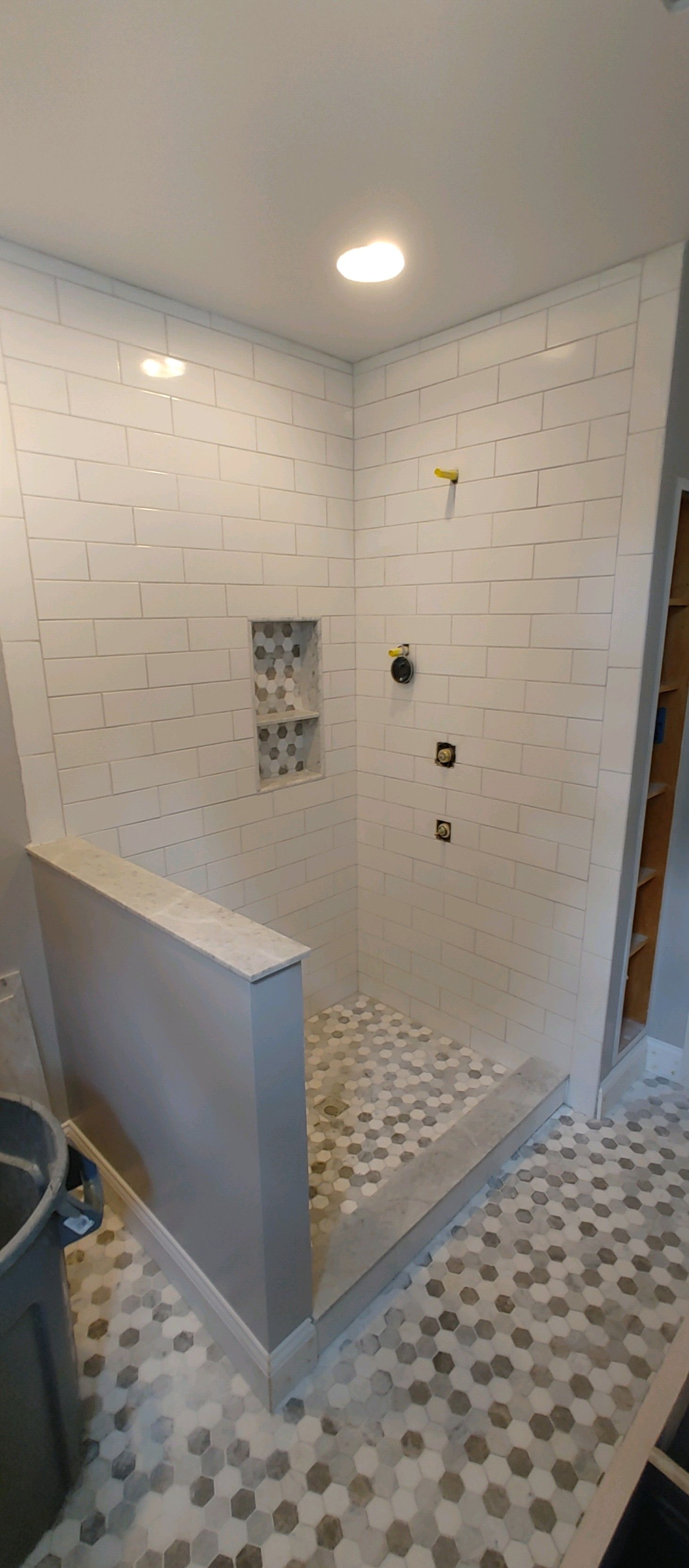A newly tiled shower with a built-in bench, pebble floor, and hexagon tile floor.