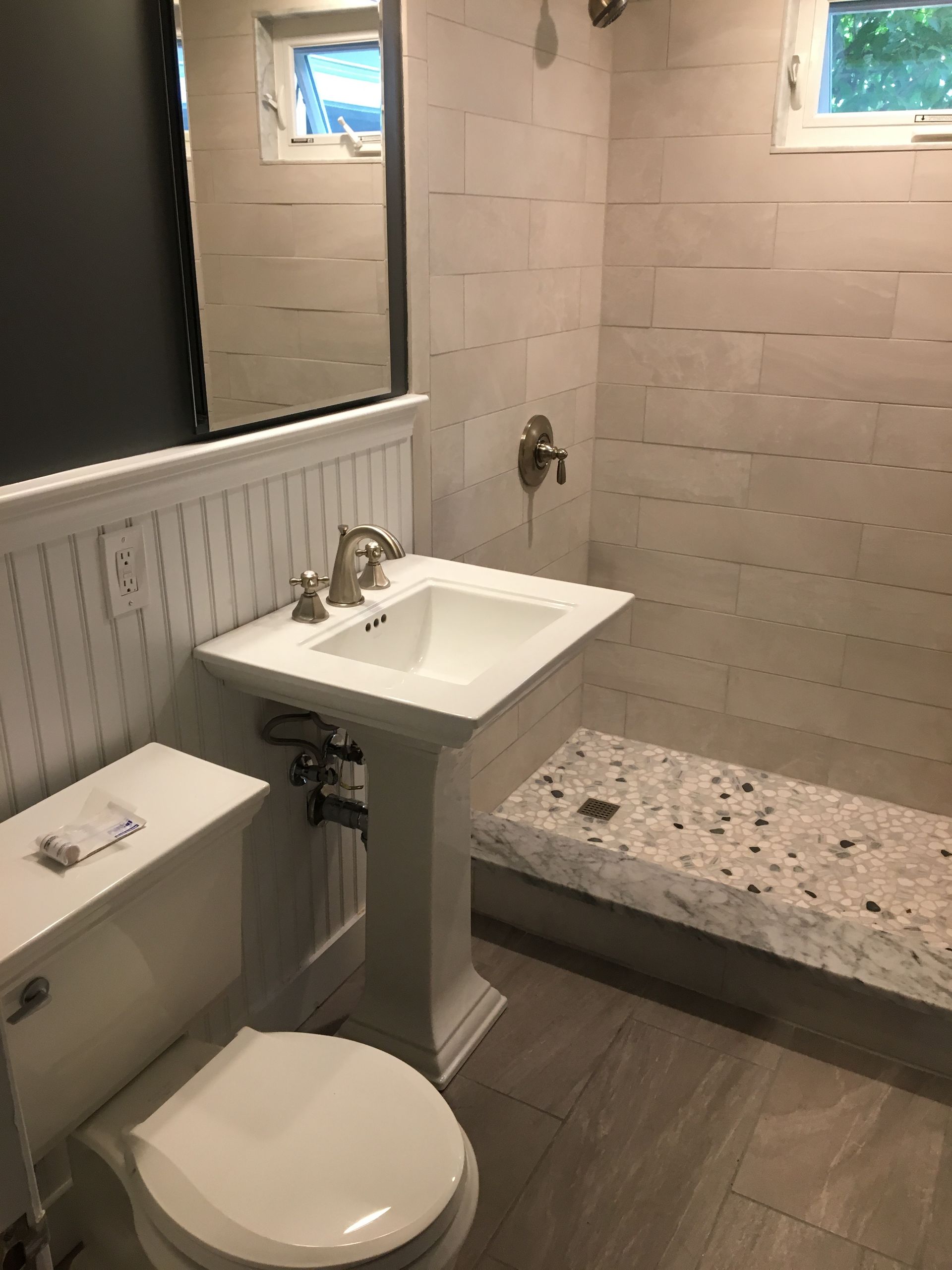 Bathroom with white pedestal sink, toilet, and tiled shower bench.