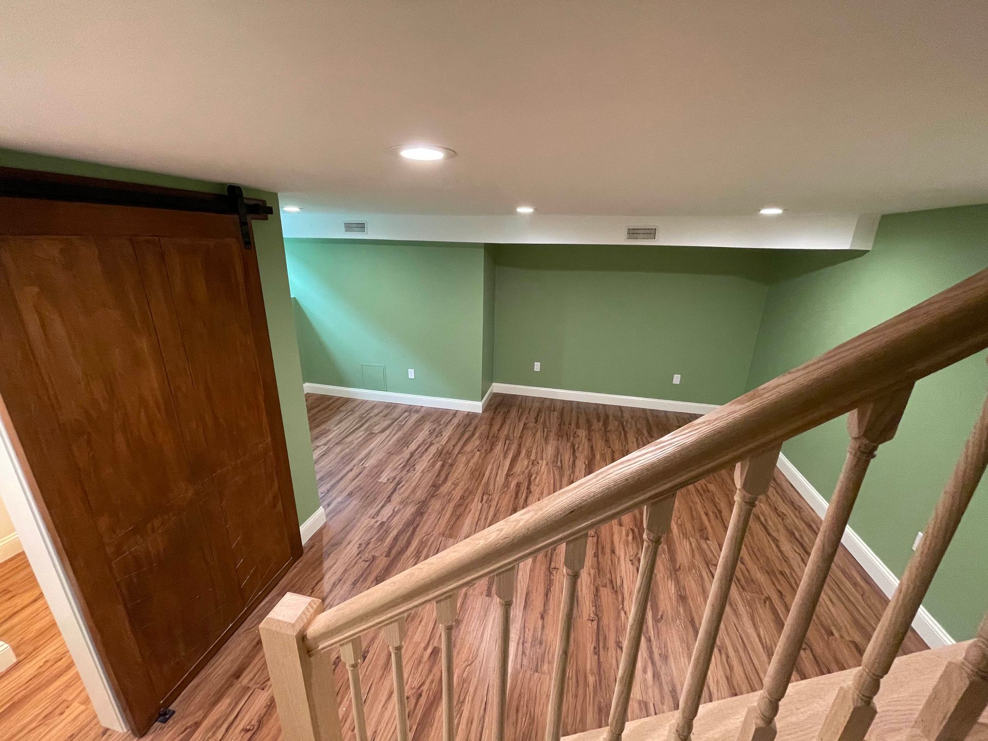 View from a staircase into a room with hardwood floors and green walls; a large wooden sliding door is on the left.