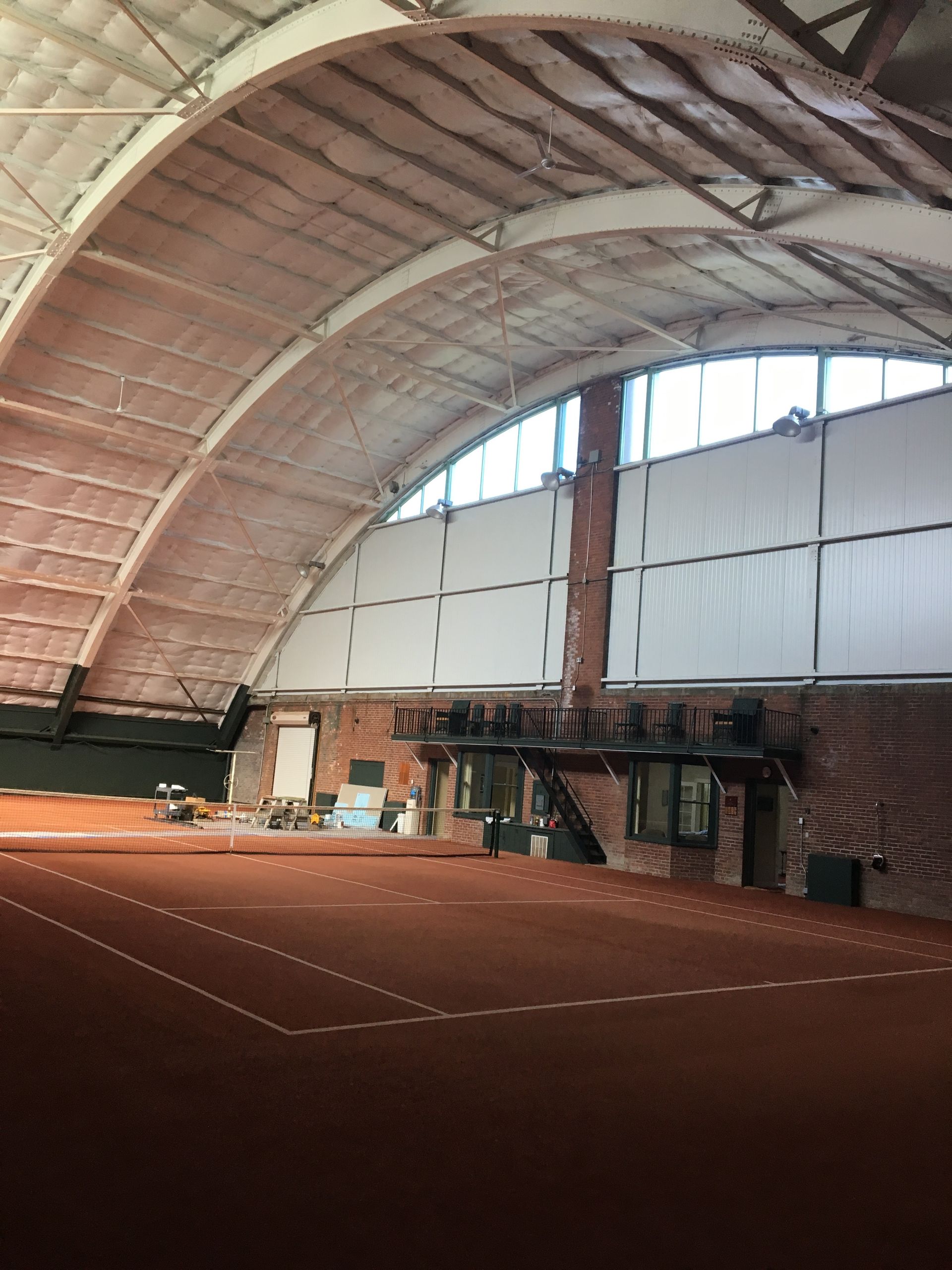 Indoor tennis court with a curved roof. Red clay court. Brick wall, white canvas covering.