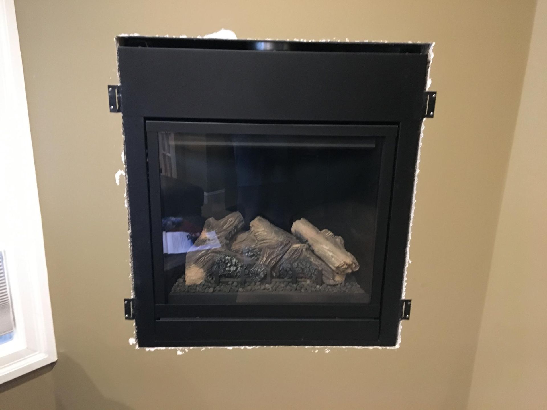Black fireplace insert installed in a tan wall, with visible logs and brackets.