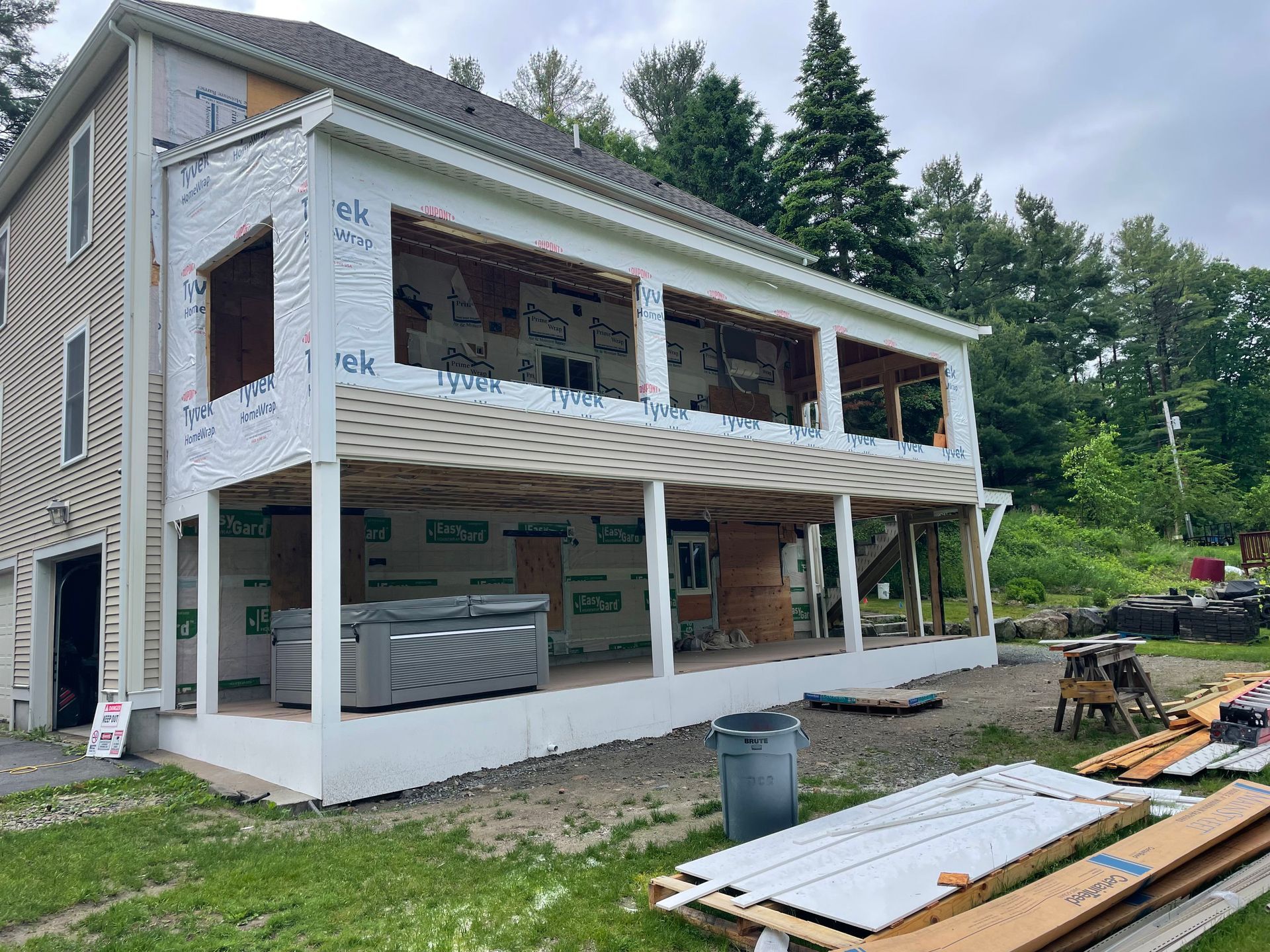 Exterior of a house under construction; white siding, wrap, open windows and a covered porch.