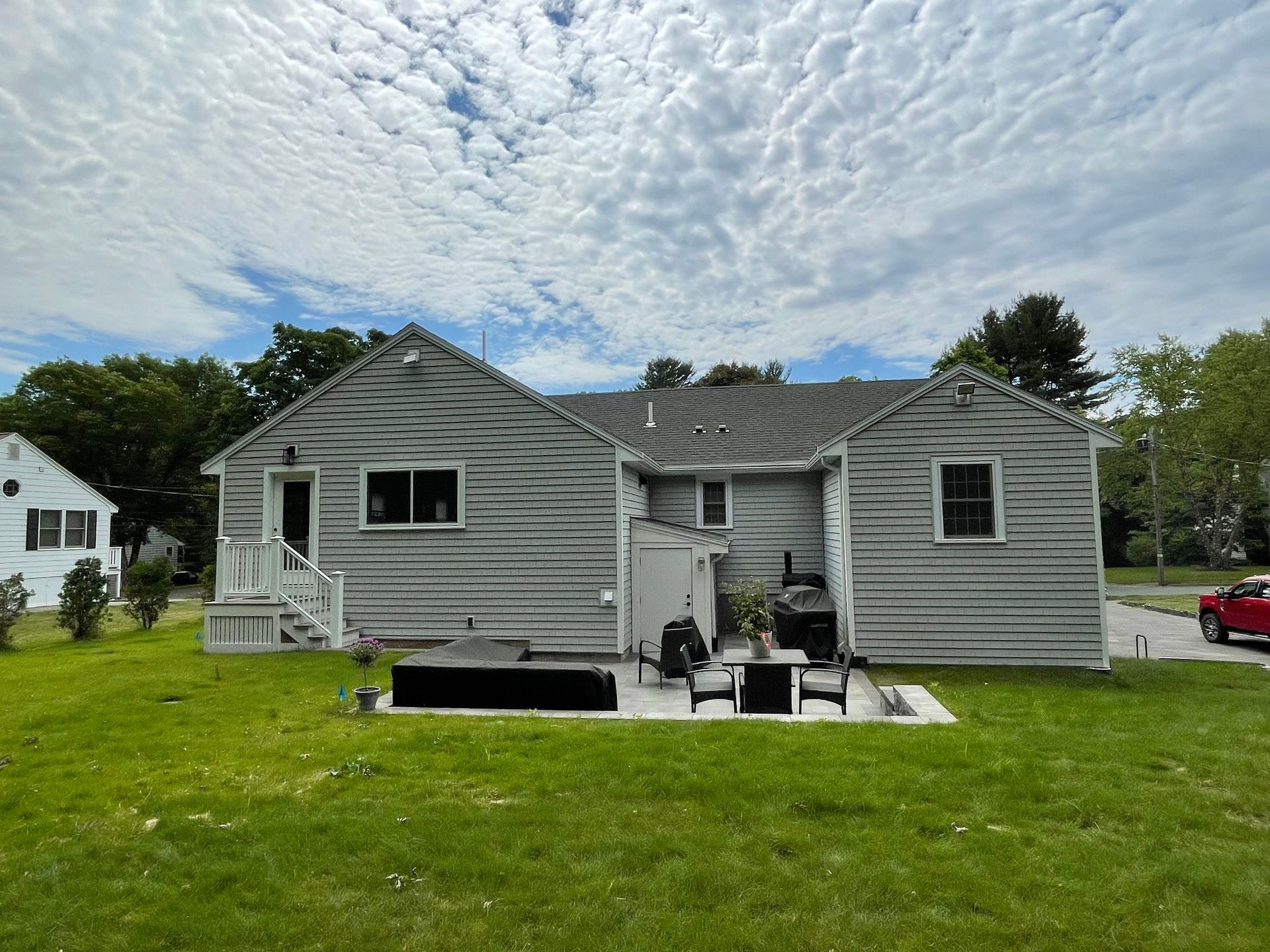 Backyard view of a house with gray siding, a patio, and a grassy lawn under a cloudy sky.
